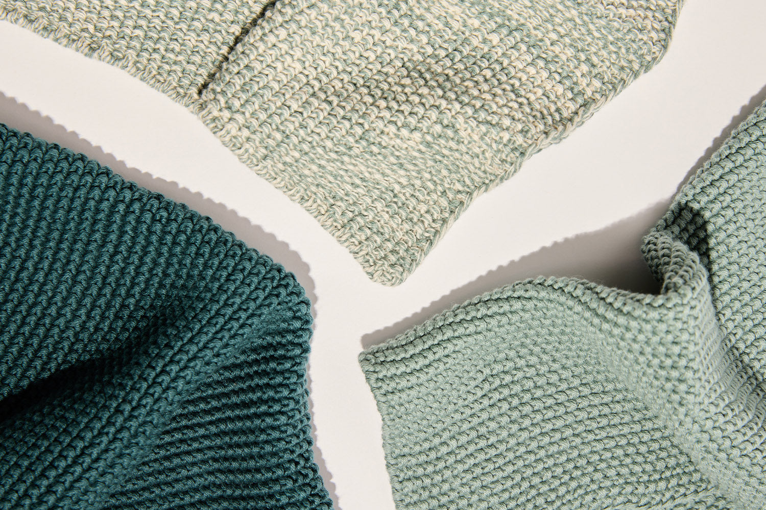 Three textured knit fabrics in shades of green and teal are arranged on a light surface, displaying different knitting patterns and soft, cozy materials.