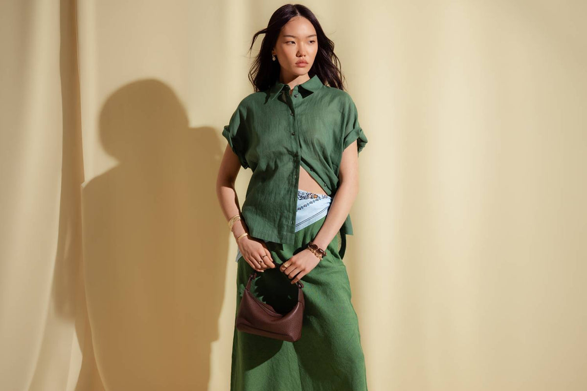 A woman wearing an oversized green shirt and a linen green slip skirt.