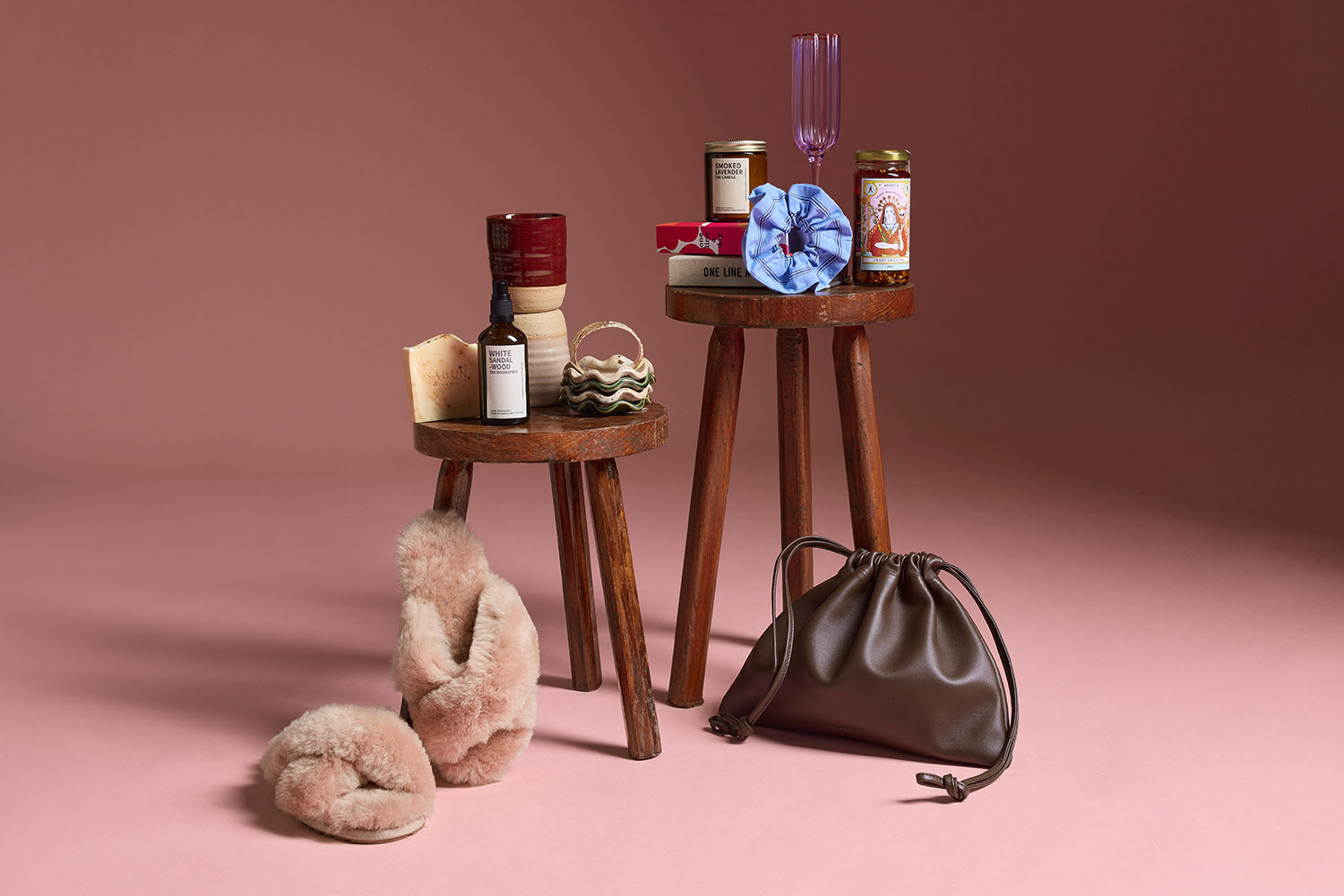 A variety of gifts on a light blue background, including handbags, a sunhat, sunglasses, mugs, candles, skincare products, books, a striped shirt, flowers, and playing cards.