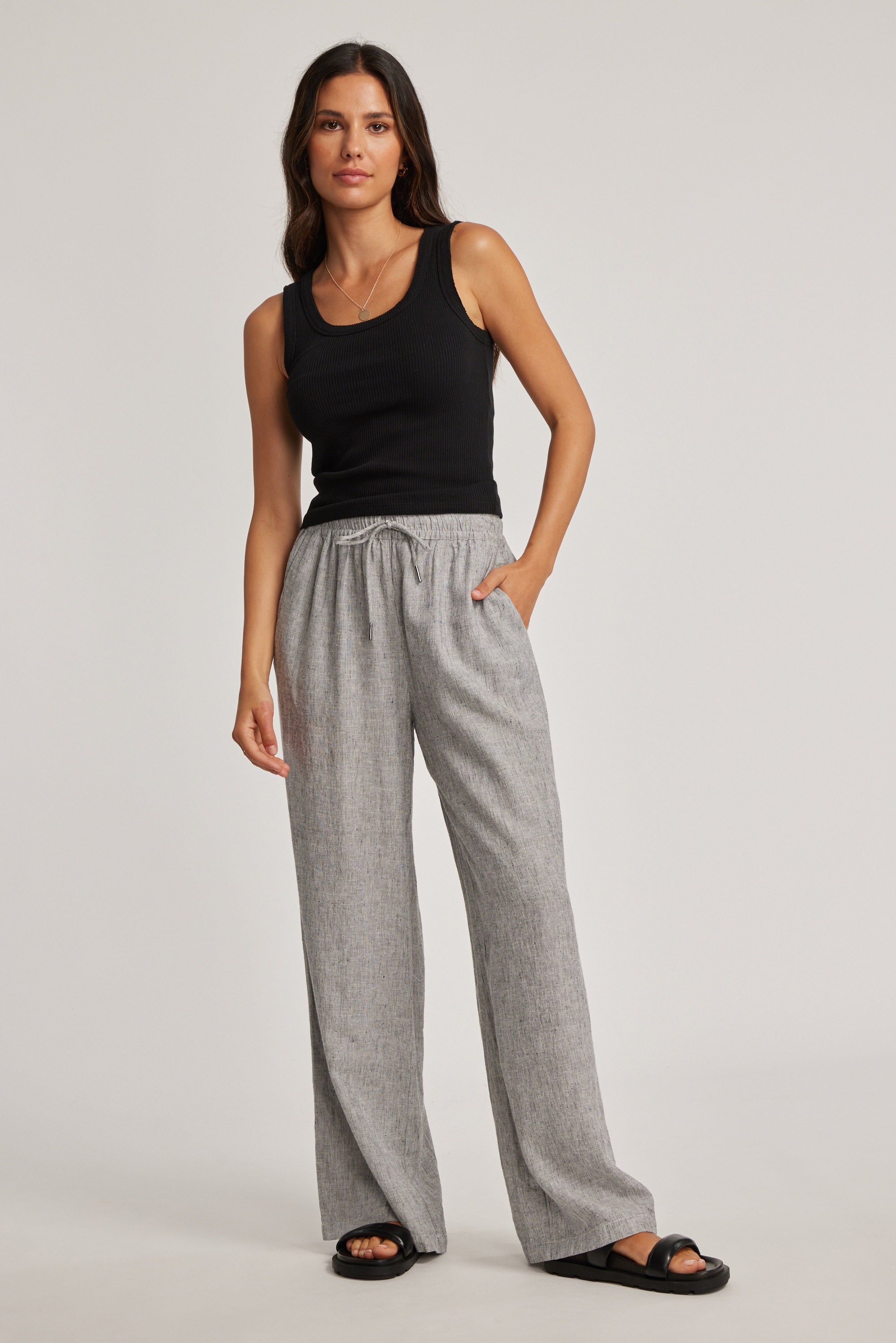 Woman wears Max's Sophie Organic Cotton Ribbed Tank, gray pants, black sandals, plain backdrop.