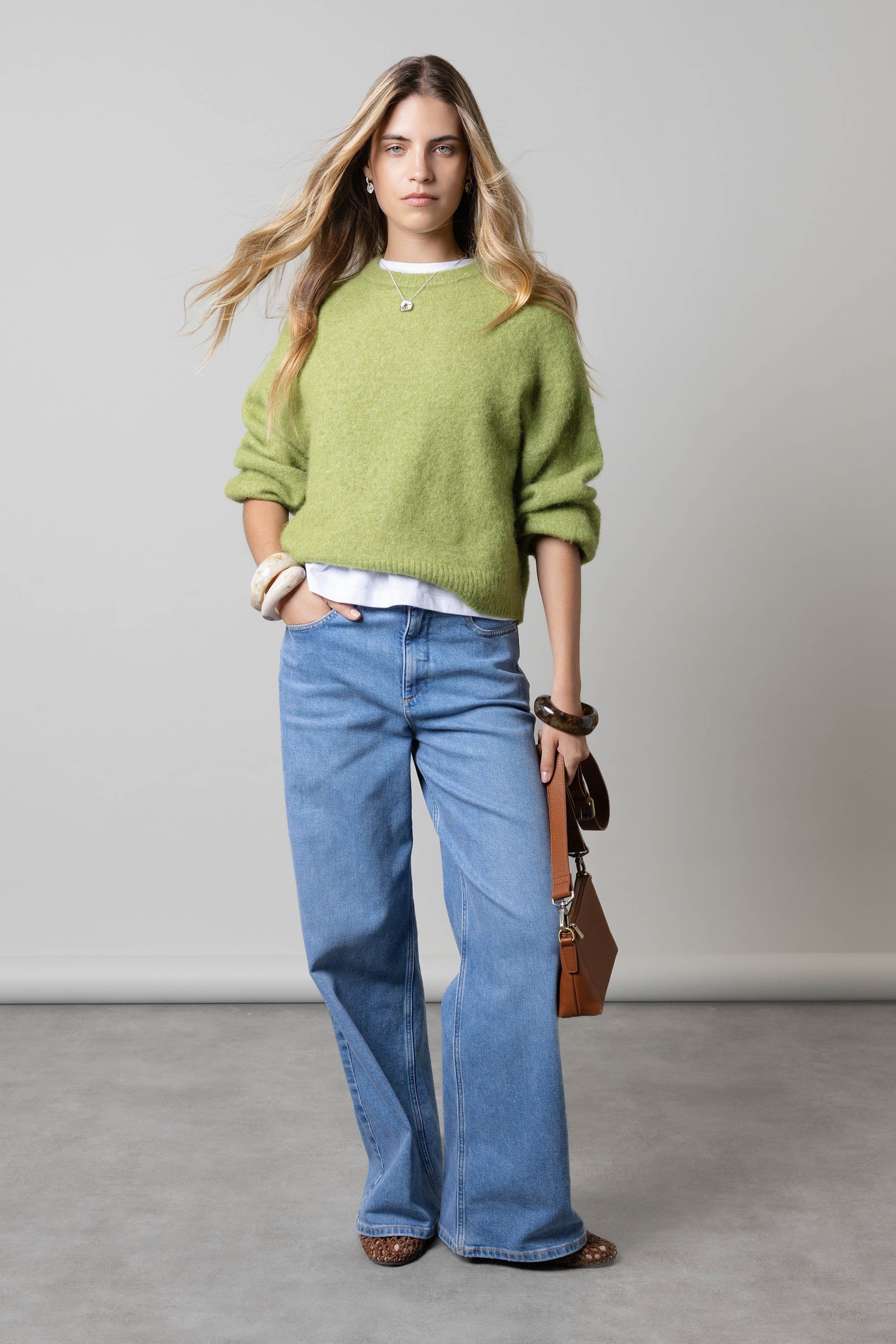 Woman in green sweater wears Max's Nevada Wide Jeans, holding a brown bag.