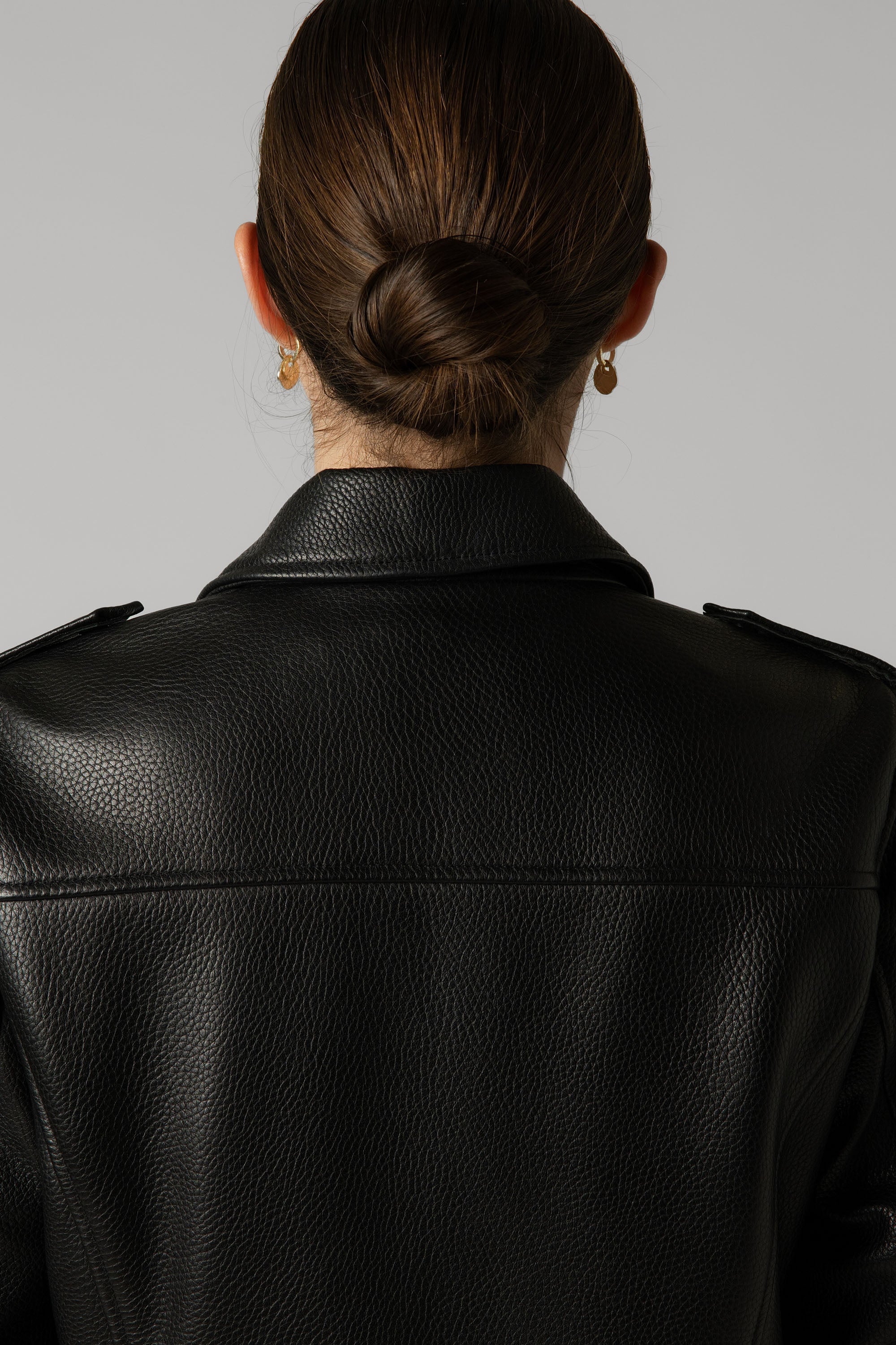 Woman with bun wears Max's The Perfect Leather Biker Jacket, seen from behind with gold hoops.