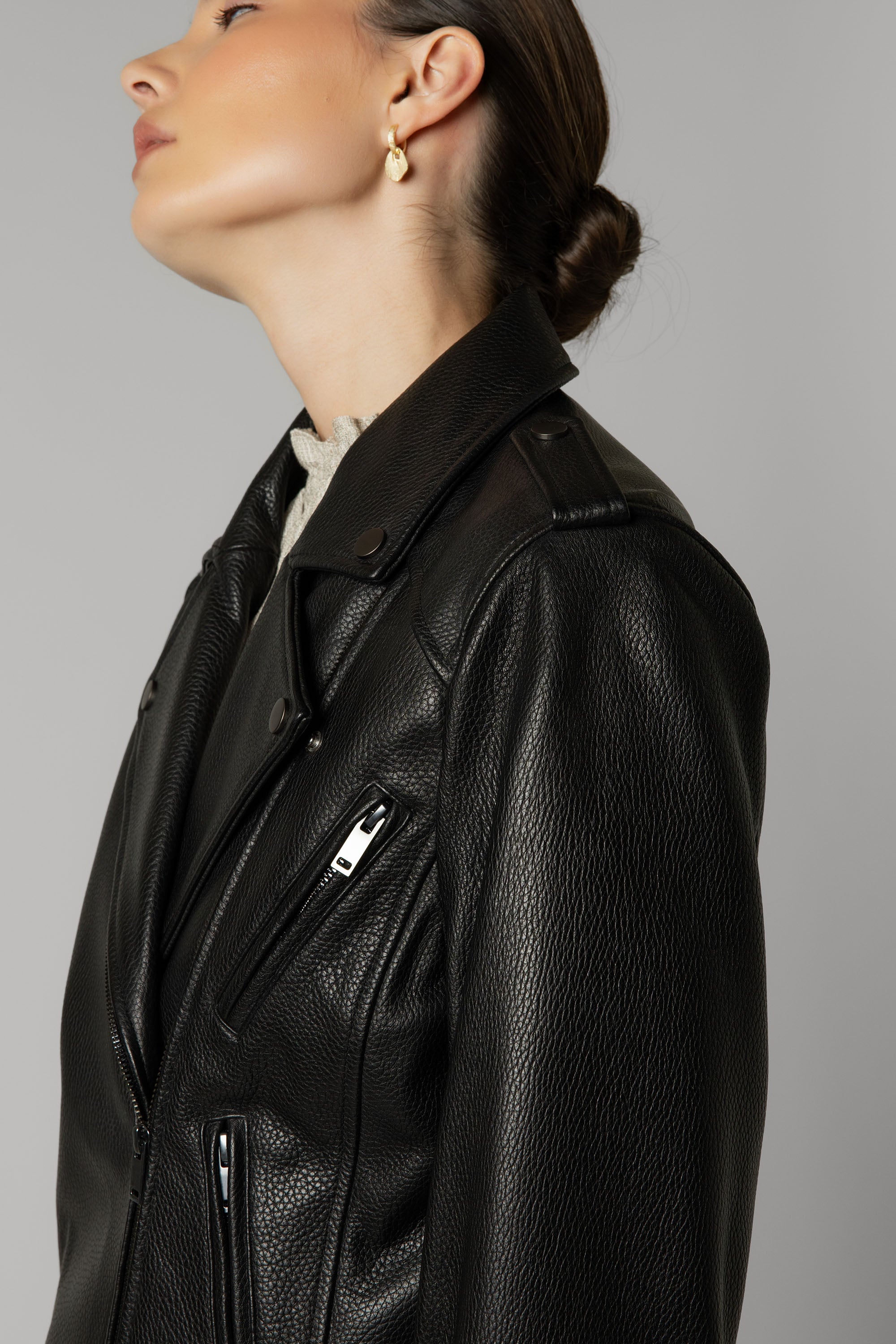 Woman in The Perfect Leather Biker Jacket by Max, pearl earring, low bun, side profile.