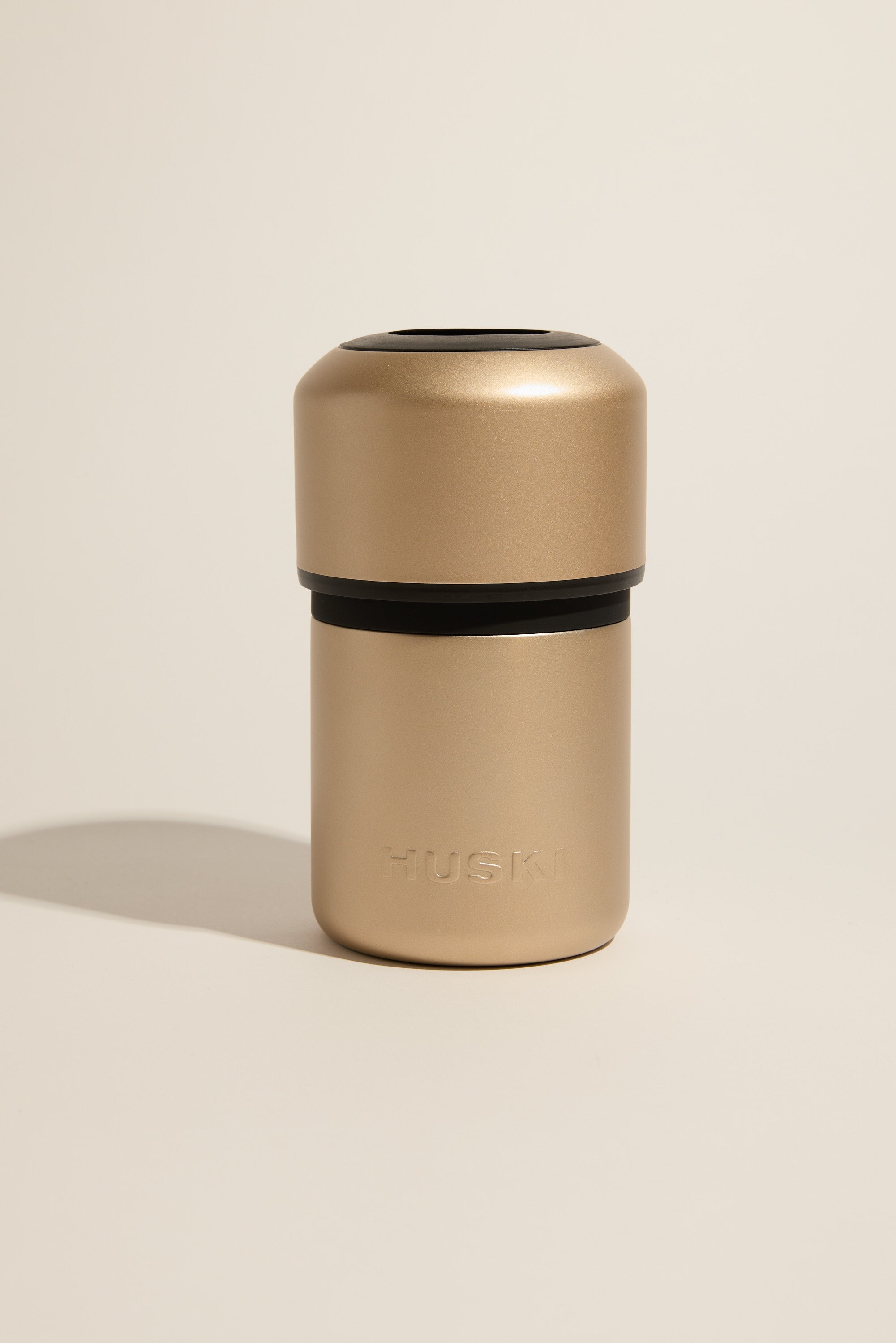 The Huski Wine Cooler by Huski, featuring a metallic gold finish and rounded top with embossed branding on the lower section, stands upright against a neutral backdrop—an elegant stainless steel cooler for any occasion.