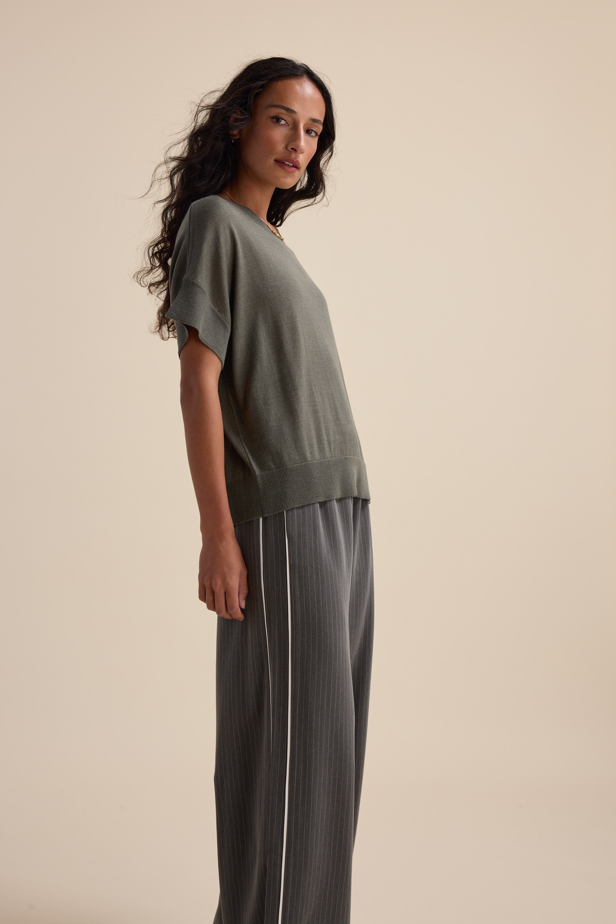 A woman in Max’s The Merino Silk Knit Tee and pinstripe pants stands against a beige background.