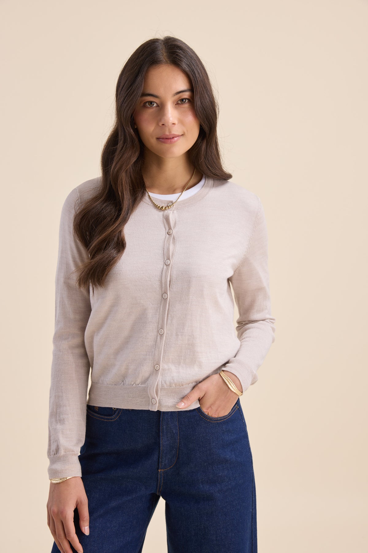 Woman wears Max’s Merino Silk Cardigan and jeans, posing against a beige backdrop, facing forward.