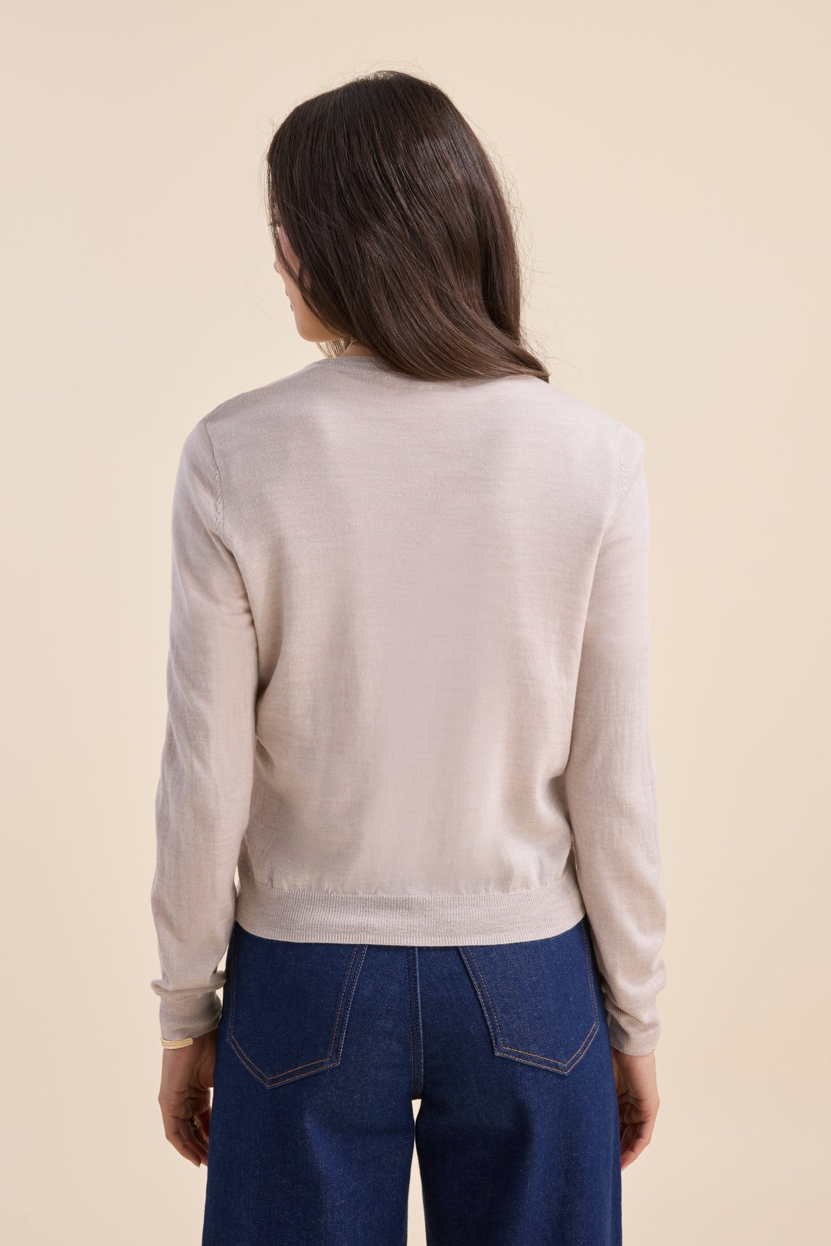 Woman in Max’s beige Merino Silk Cardigan and blue jeans, facing away on a beige background.