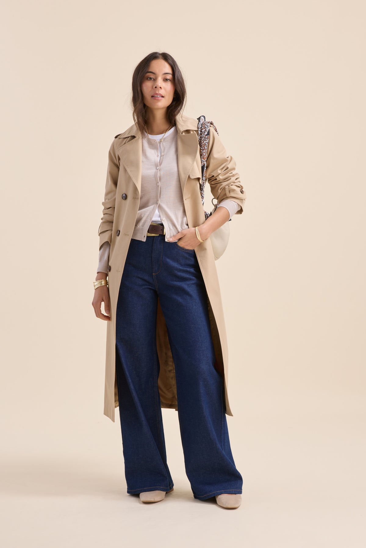 Woman in beige trench, white top, wide jeans, holding Max’s Merino Silk Cardigan and white purse.