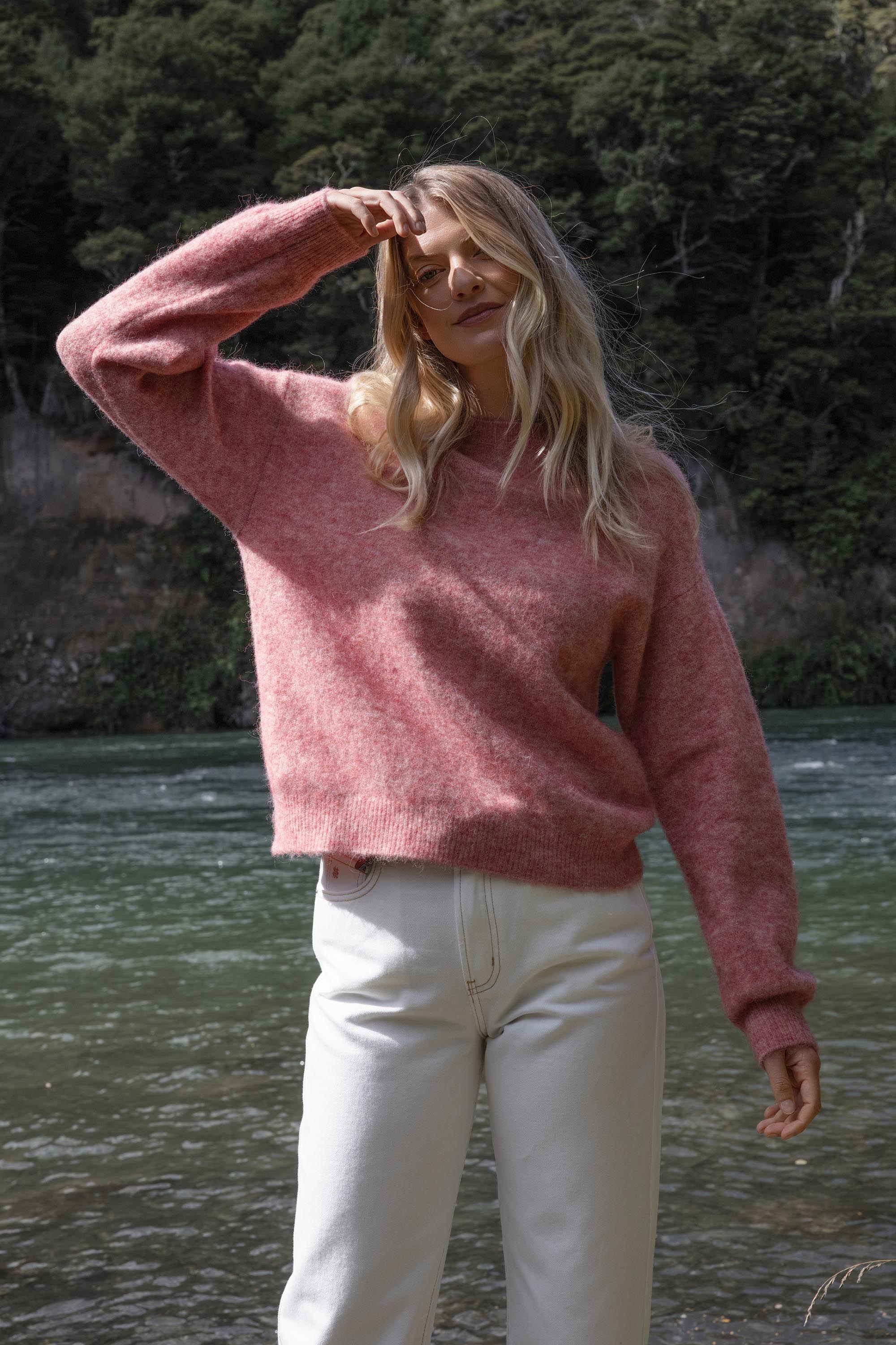 Woman in Max Hayley Luxe Whisper Crew Neck Sweater and white pants stands by a riverside.