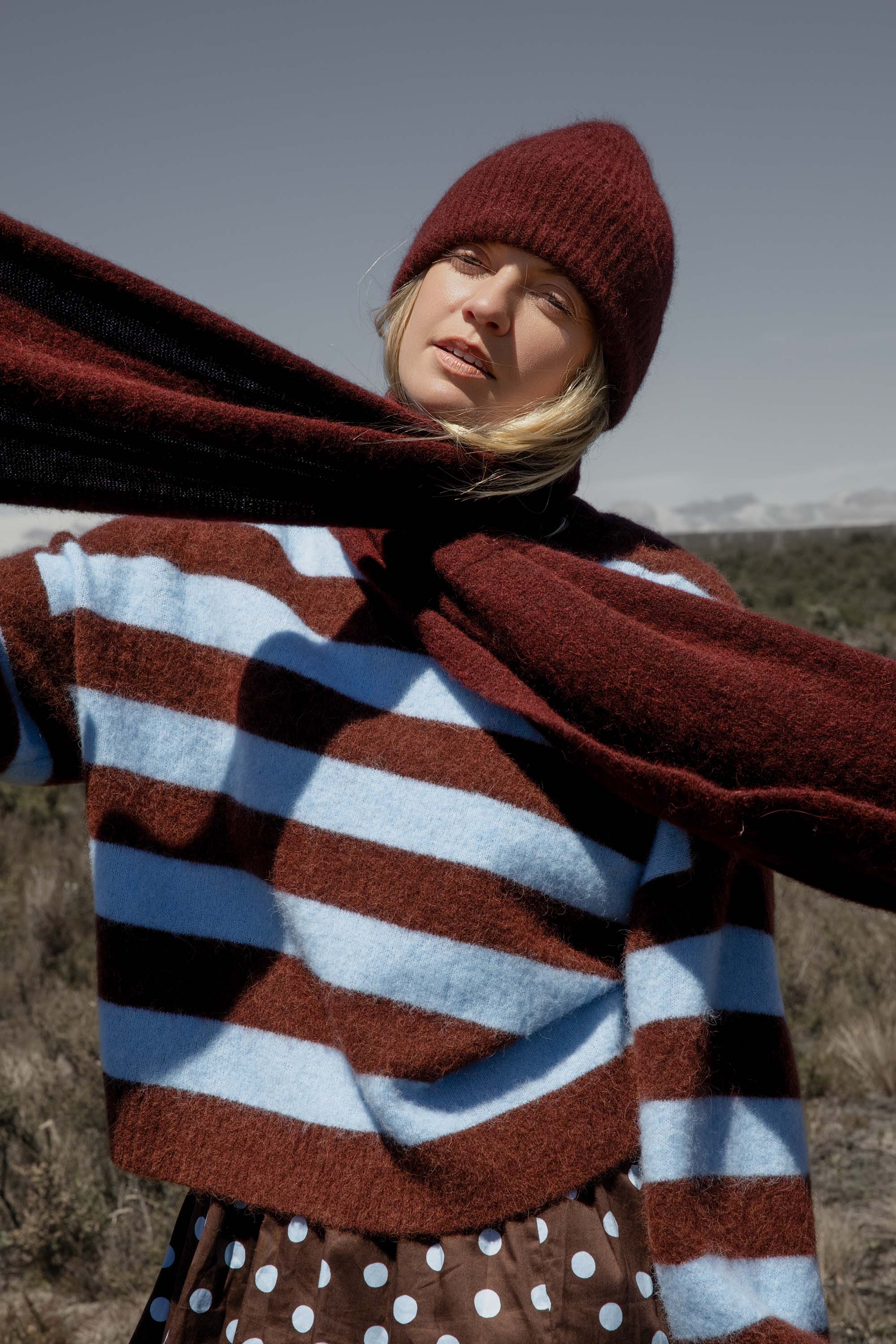 Woman in striped sweater, polka dot skirt, maroon hat, and Max Hailey Luxe Whisper Knit Scarf outdoors.