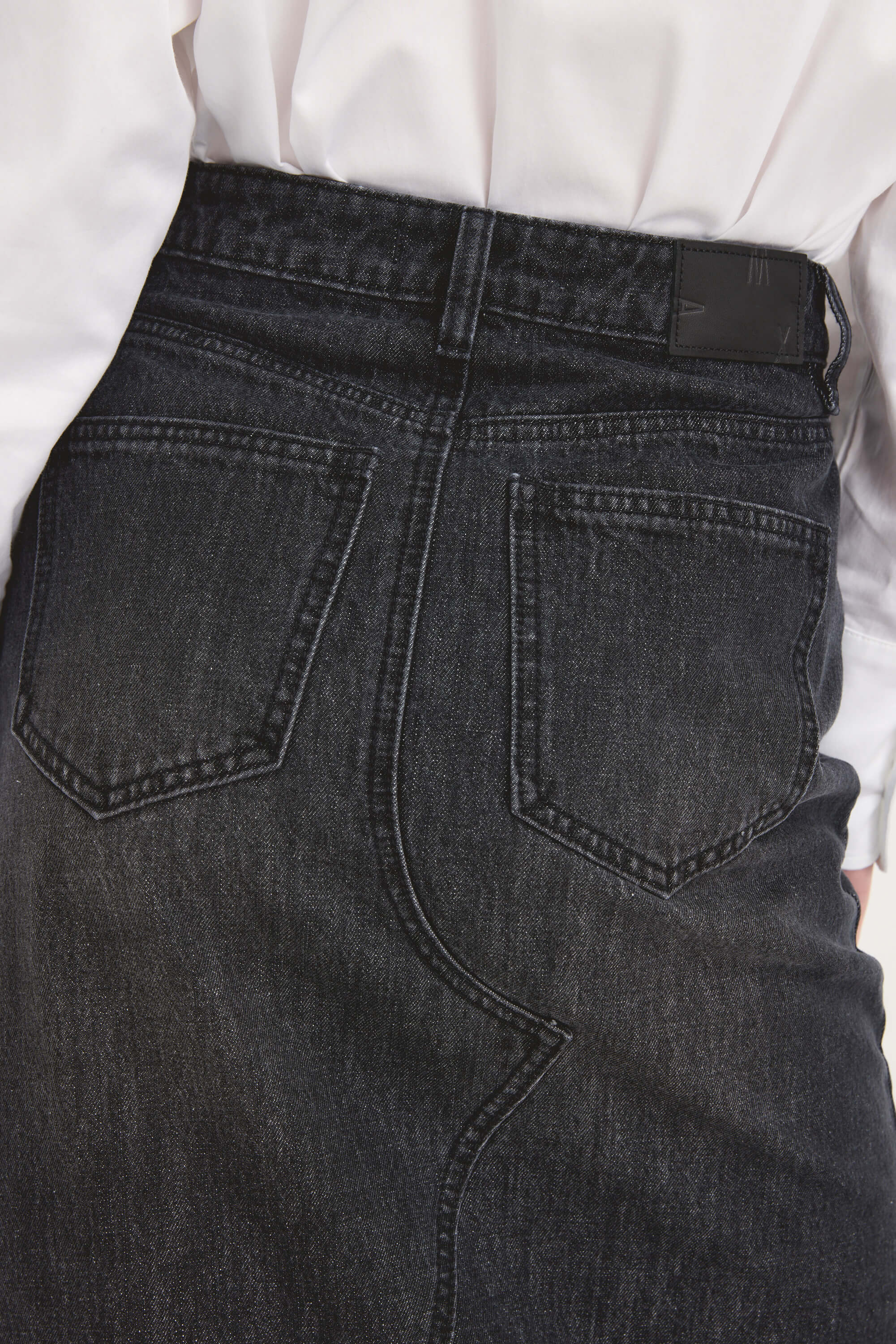 Close-up of a person in a white shirt tucked into the Max Paris Maxi Denim Skirt, made from eco denim, highlighting the skirt's high rise fit, back pockets, and waistband.