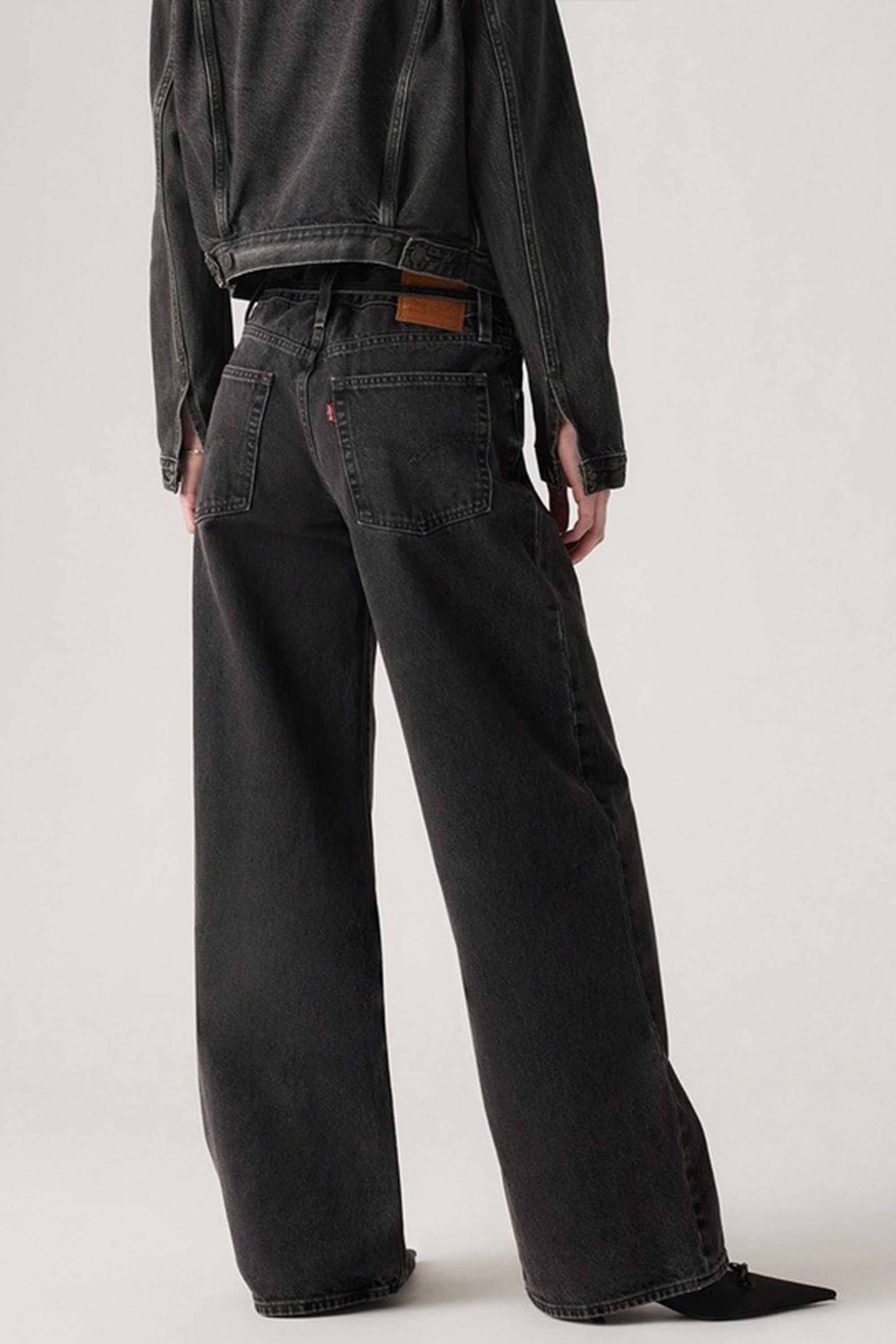 A person stands with their back to the camera against a plain light background, wearing Levi's XL Straight Jeans featuring a brown waistband patch and a black denim jacket.