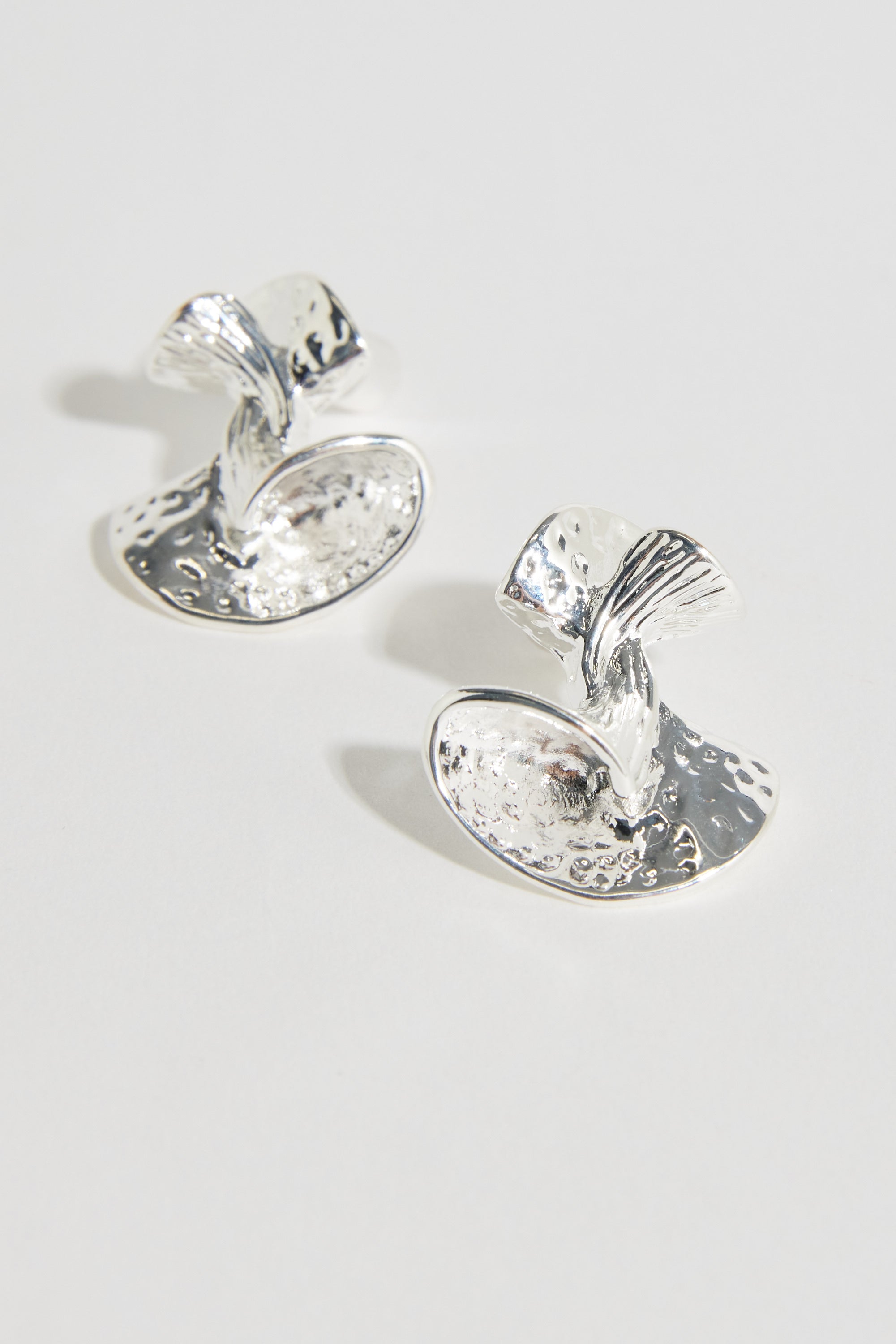 The Bela Sonder Monroe Earrings by Bela Sonder feature abstract, sculptural shapes with a hammered texture, crafted from recycled brass and sterling silver posts, shown on a light background.