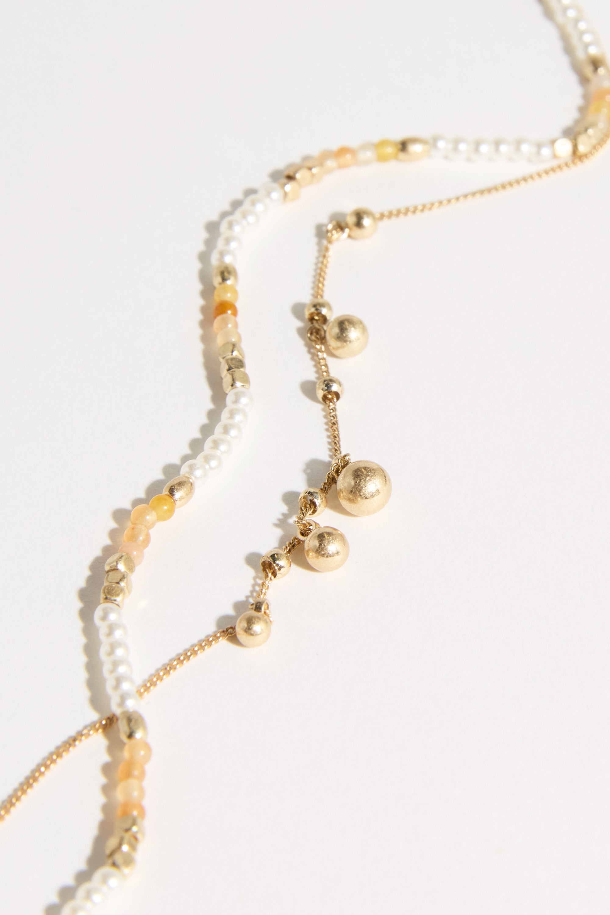 A close-up of Bela Sonder Kaia Necklace pieces with small pearls, gold beads, tiny chains, and light yellow stones, elegantly arranged on a white background.