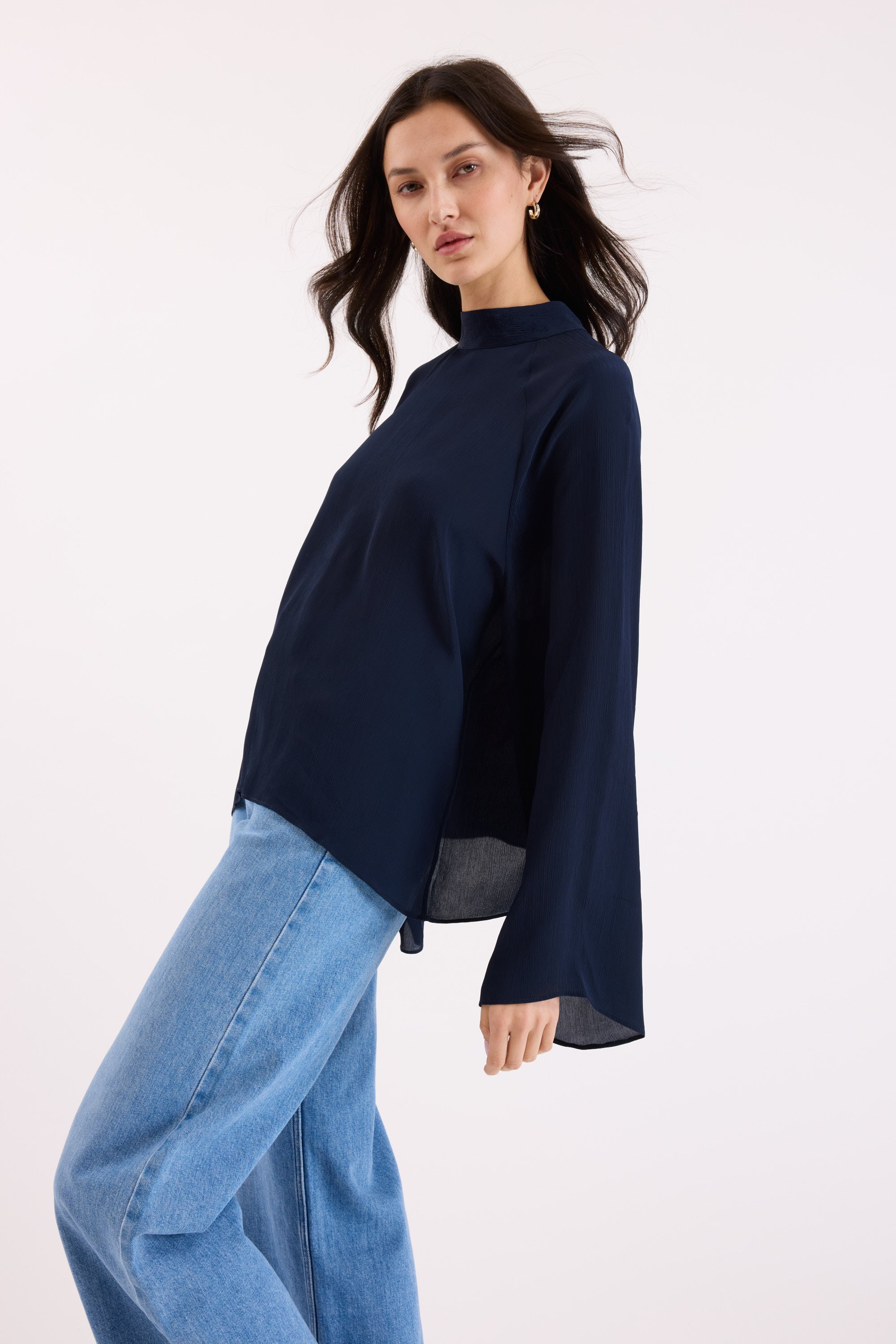 A woman with long dark hair wears the Max Lindsay Textured Blouse with flared sleeves and light blue jeans, posing against a plain light background.