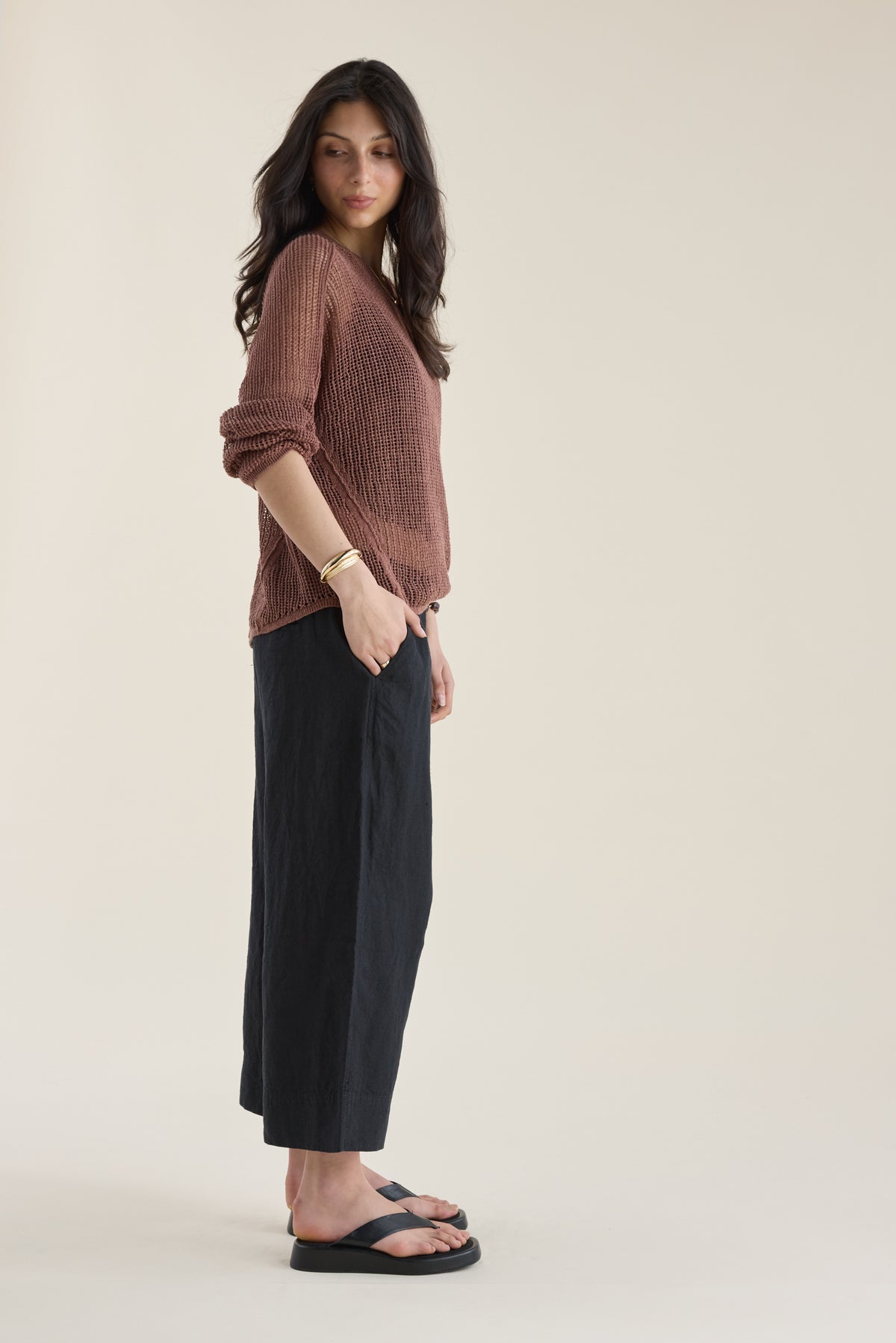 Woman in brown top and Elementary High Tide Linen Crop Pants stands sideways against plain backdrop.