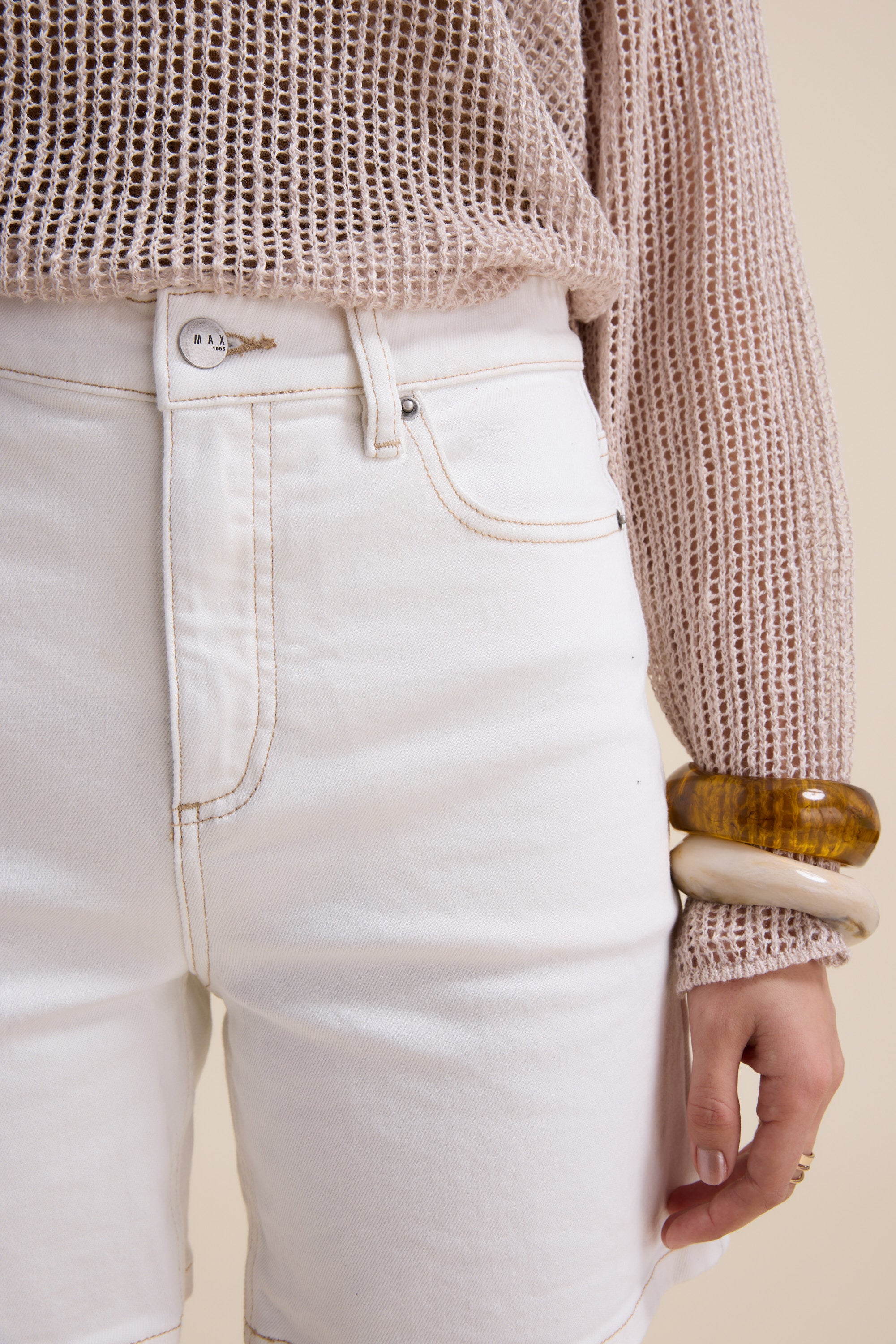 A person wearing Max’s The Effortless Denim Short in white and a loose-knit beige sweater, accessorized with two chunky bangles—one brown, one cream. The image is cropped to the torso and upper legs.
