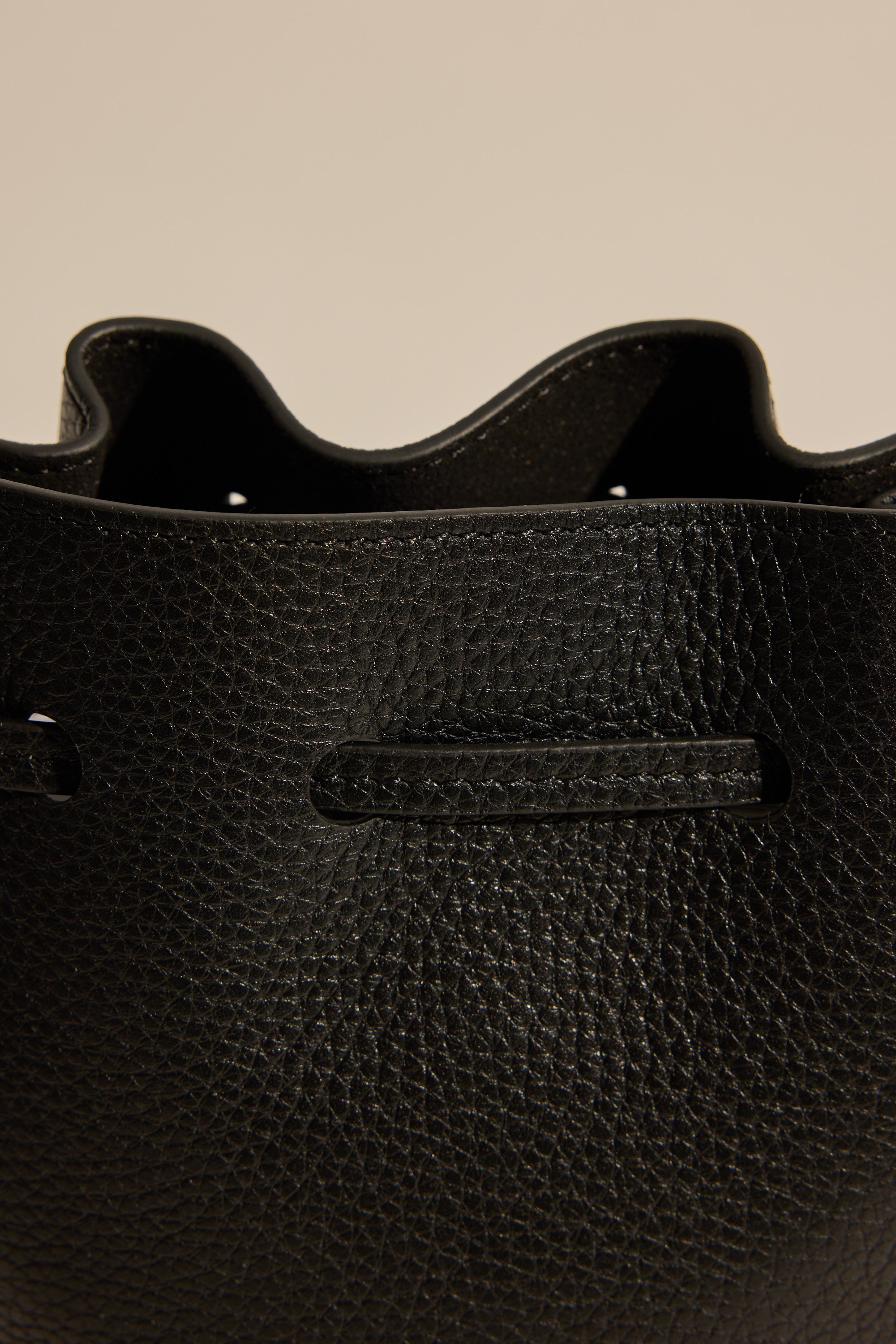 Close-up of the upper part of The Horse Bob Bucket by The Horse, featuring black grained leather, visible stitching, and a wavy open top edge set against a neutral background.