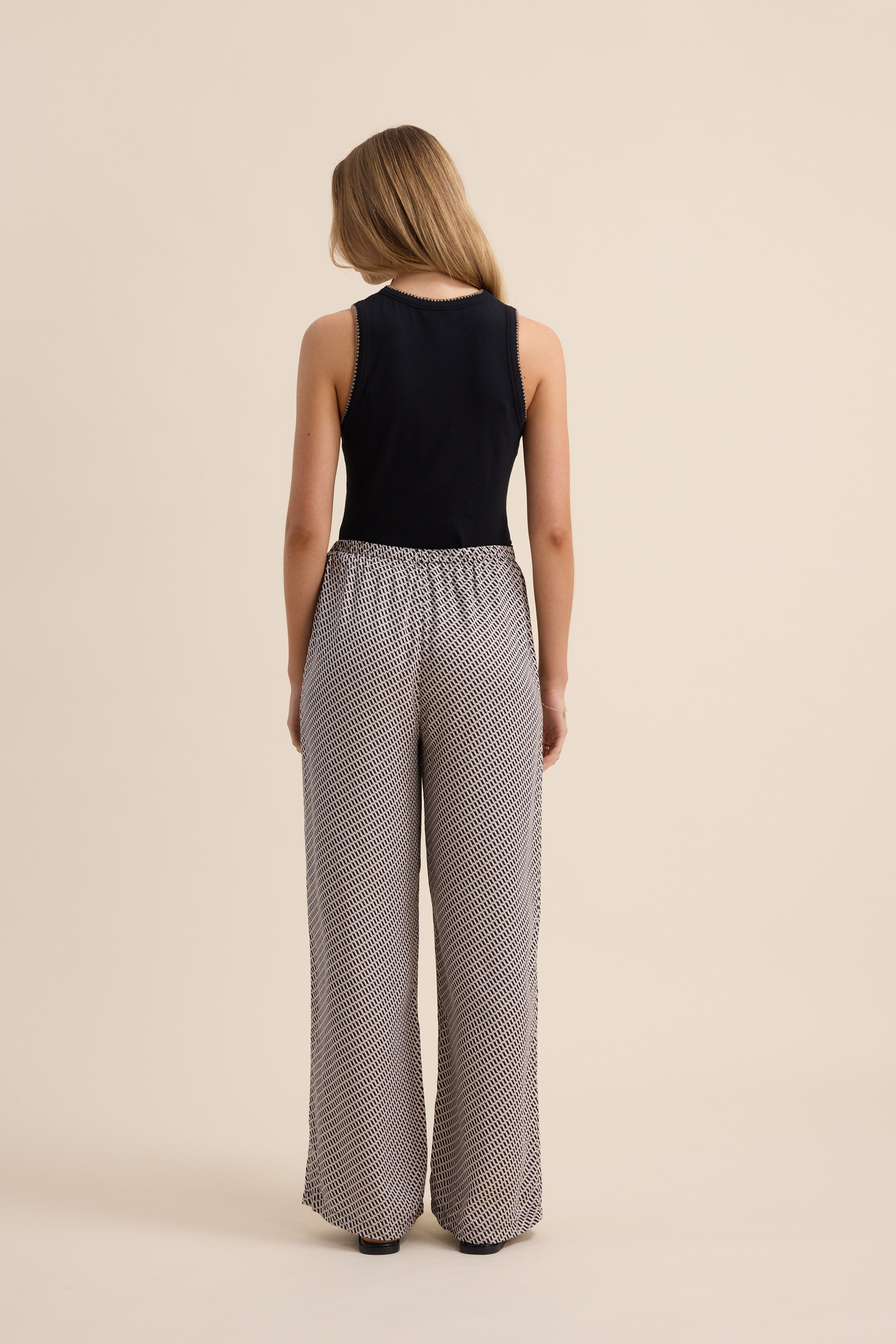 Woman in black sleeveless top and Max's The Luxe Pants, cupro blend, back to camera.