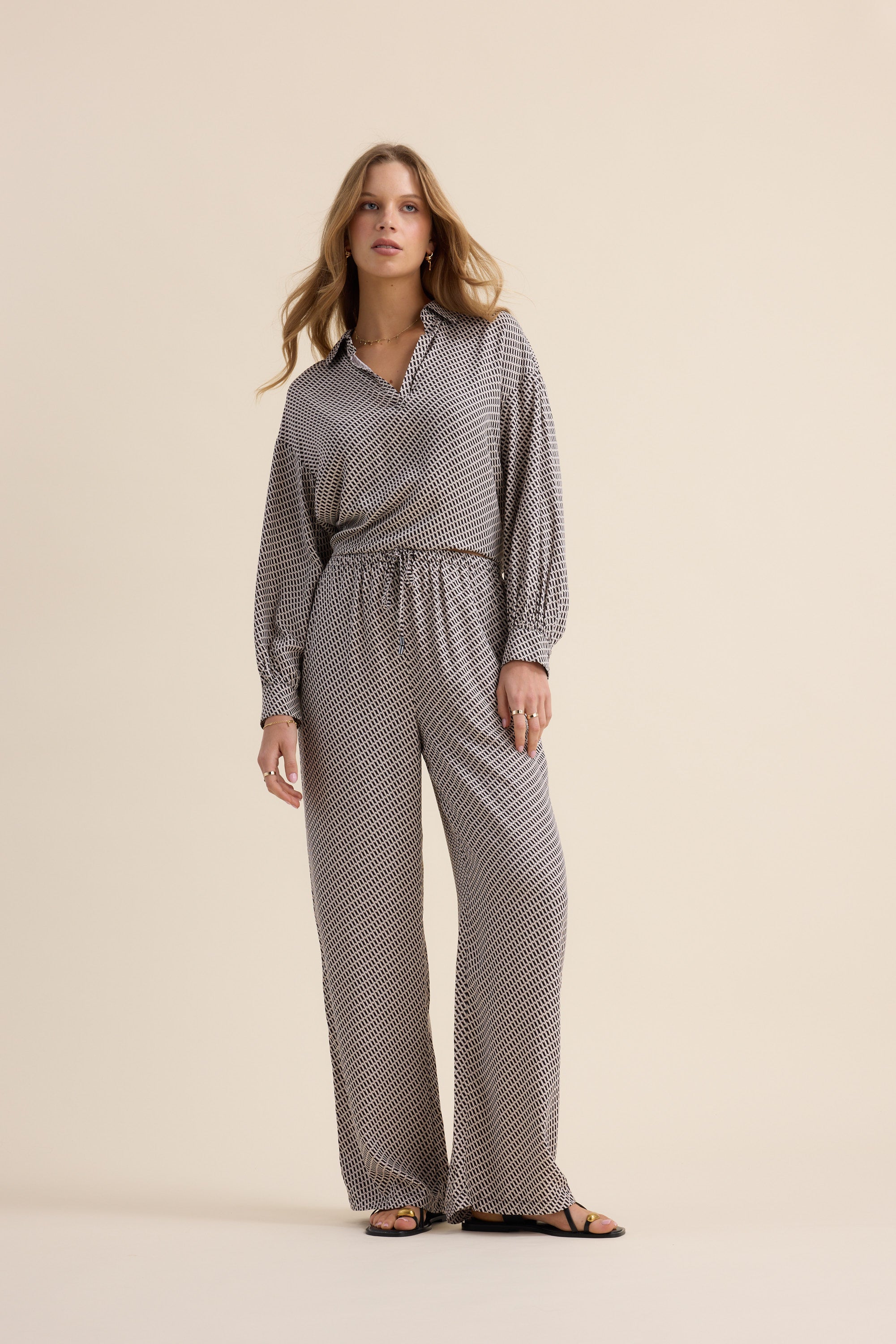 Woman in The Luxe Pants by Max and sandals, standing against a beige background.