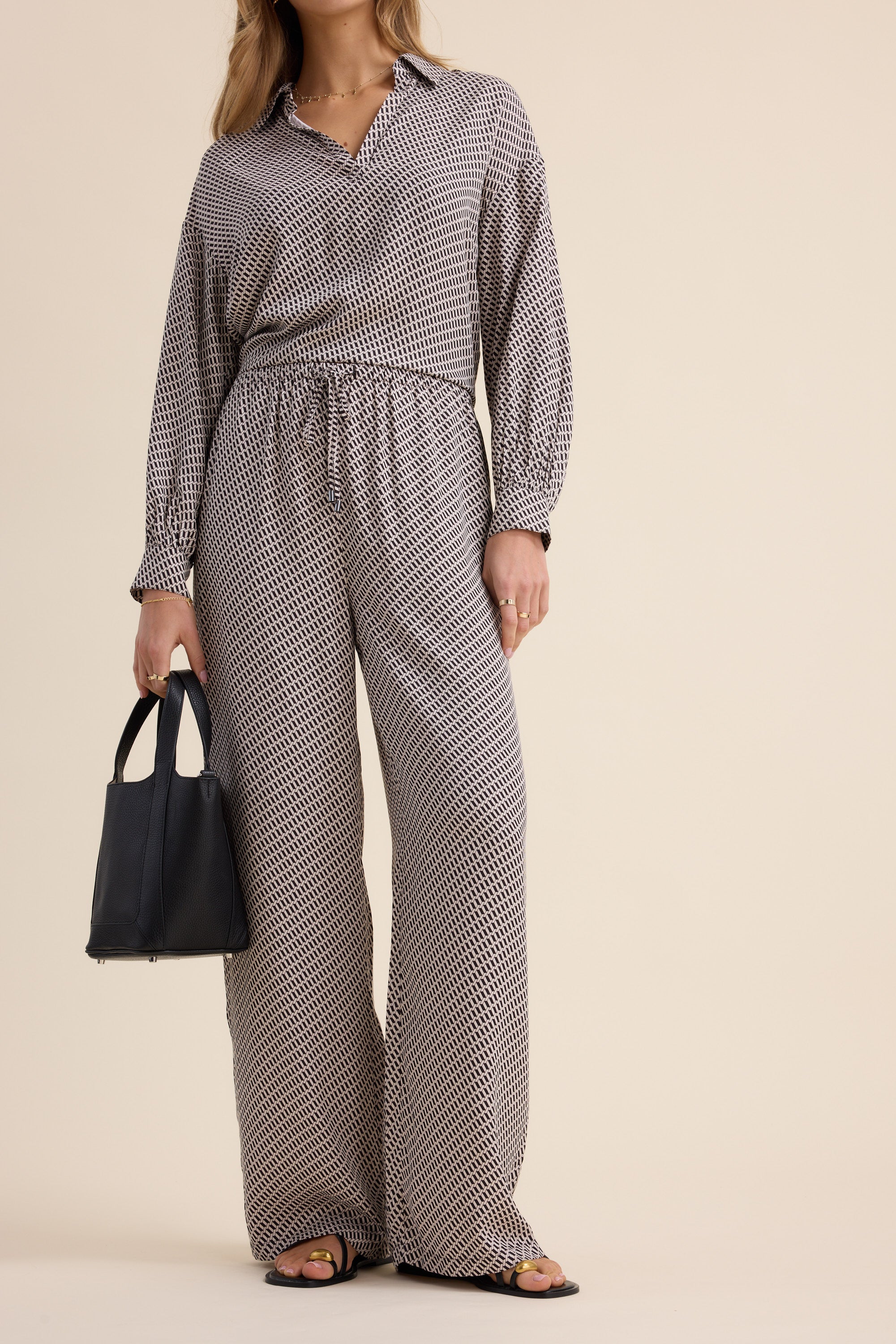 Woman in The Luxe Pants by Max, holding a black handbag and wearing sandals.