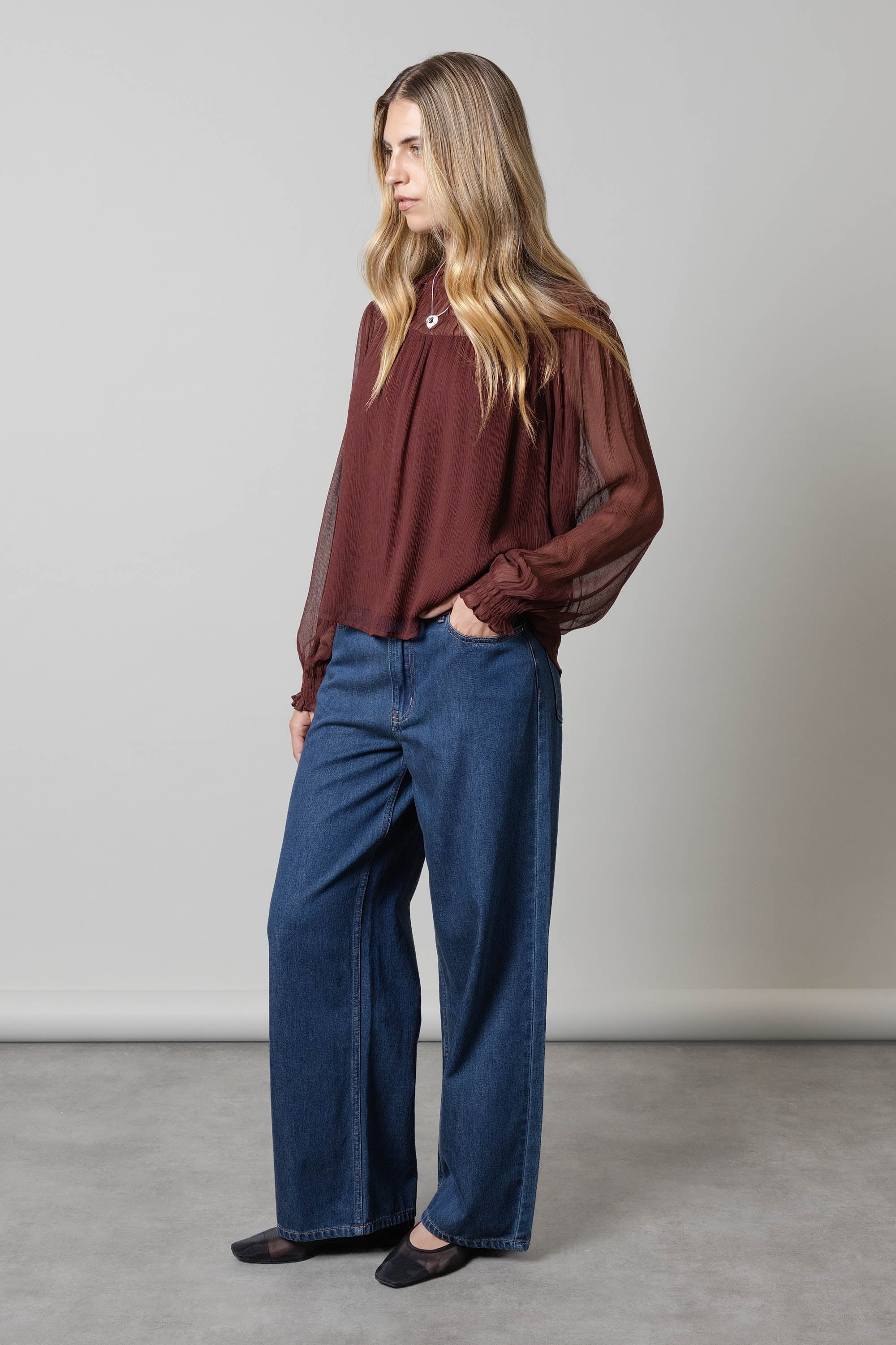 Woman in Aspen Wide Leg Jeans by Max and a sheer maroon blouse against a plain background.