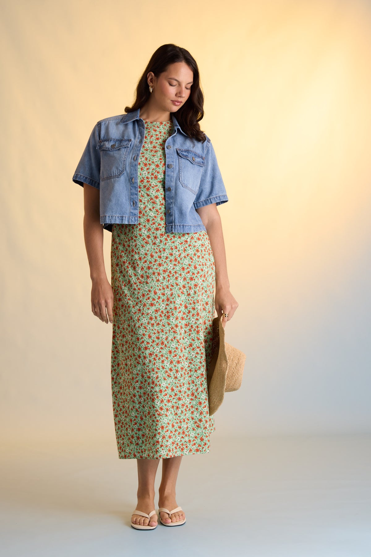 Woman in Max Poppy Short Sleeved Dress, denim jacket, holding hat, sandals, light background.