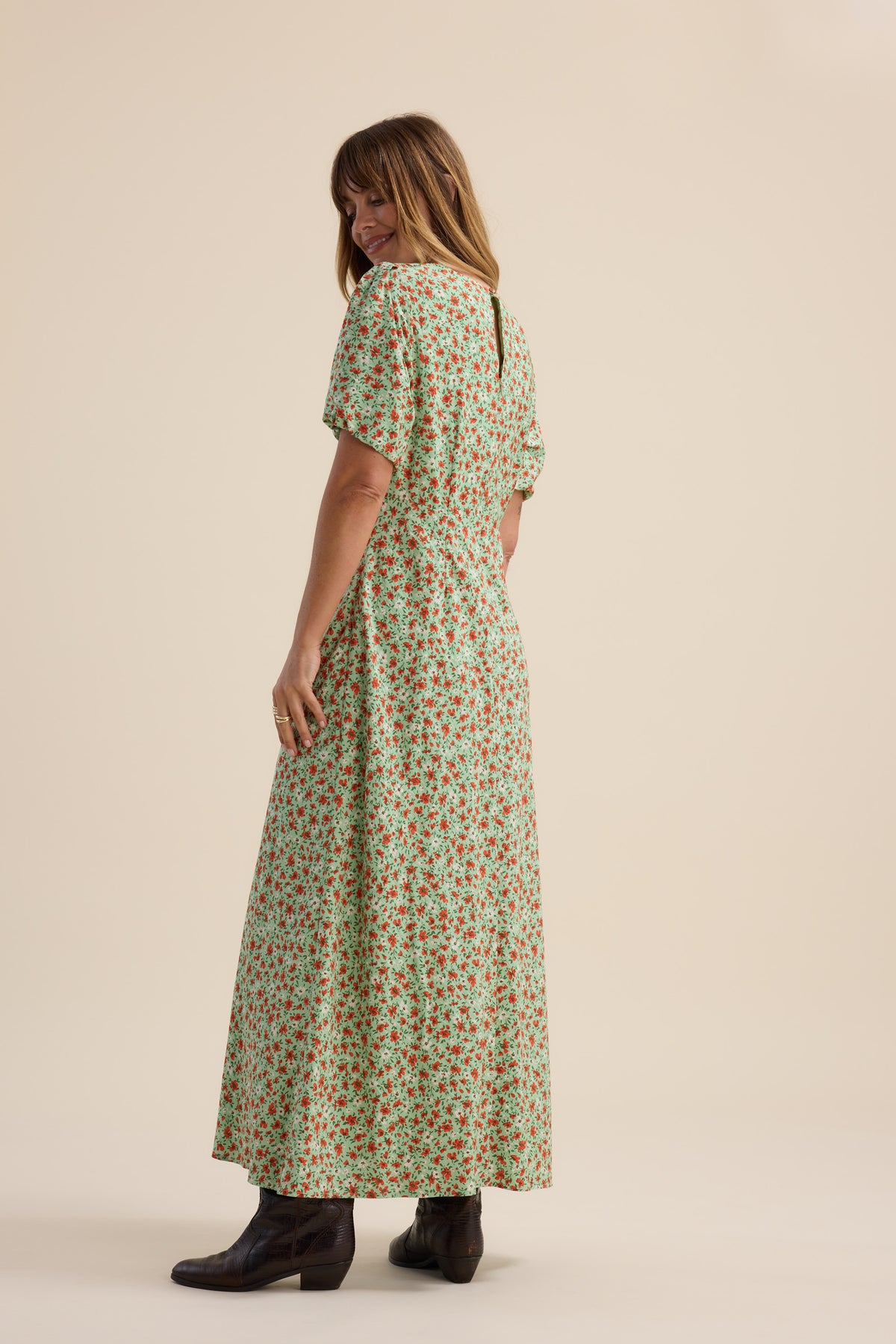 Woman in Max’s Poppy Short Sleeved Dress and black boots stands, turned slightly, smiling.