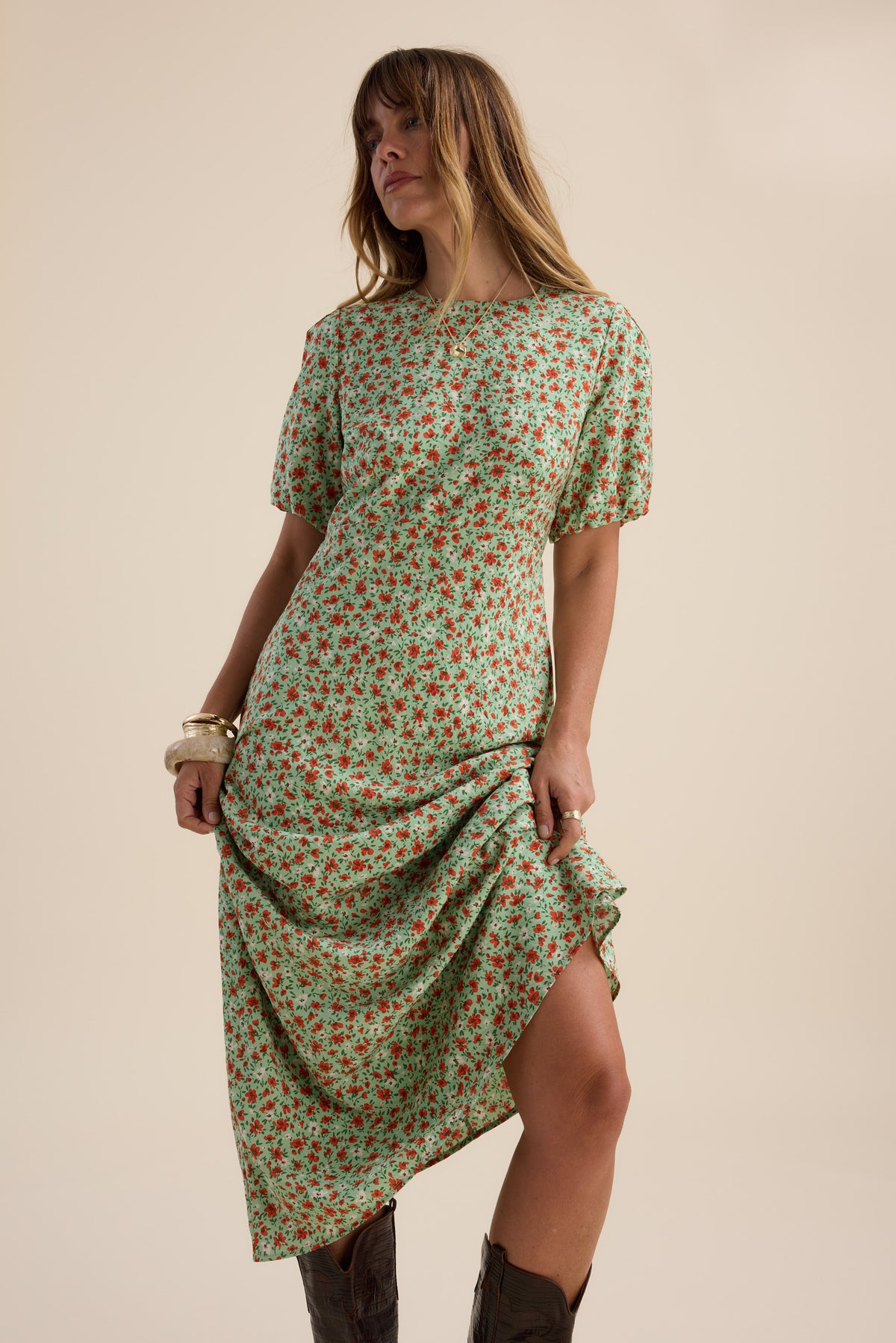 Woman wears Max Poppy Short Sleeved Dress, posing with one knee bent in brown boots and bracelets.