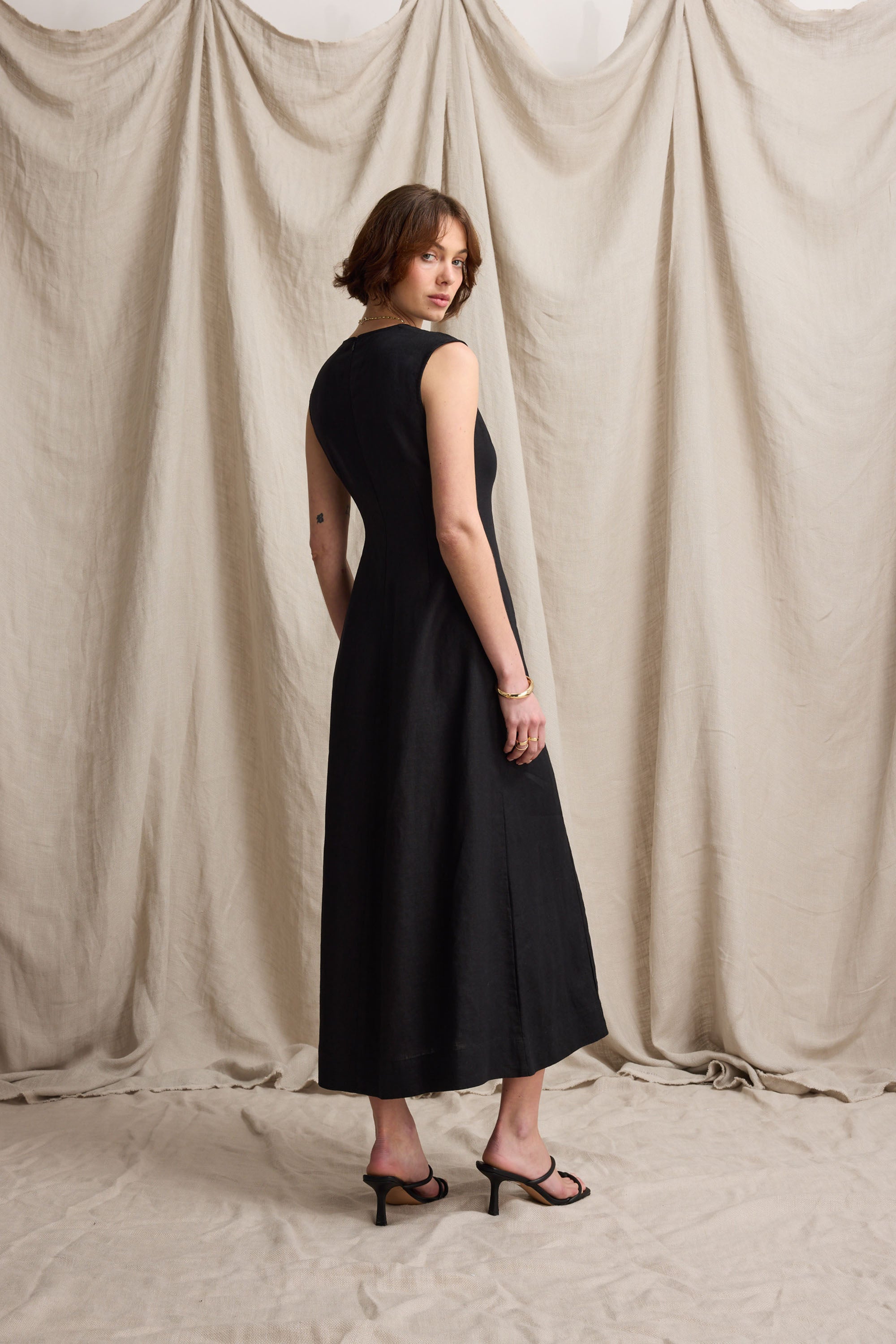 Woman in the Max Alice V Neck Linen Dress and heels stands by a beige draped backdrop.