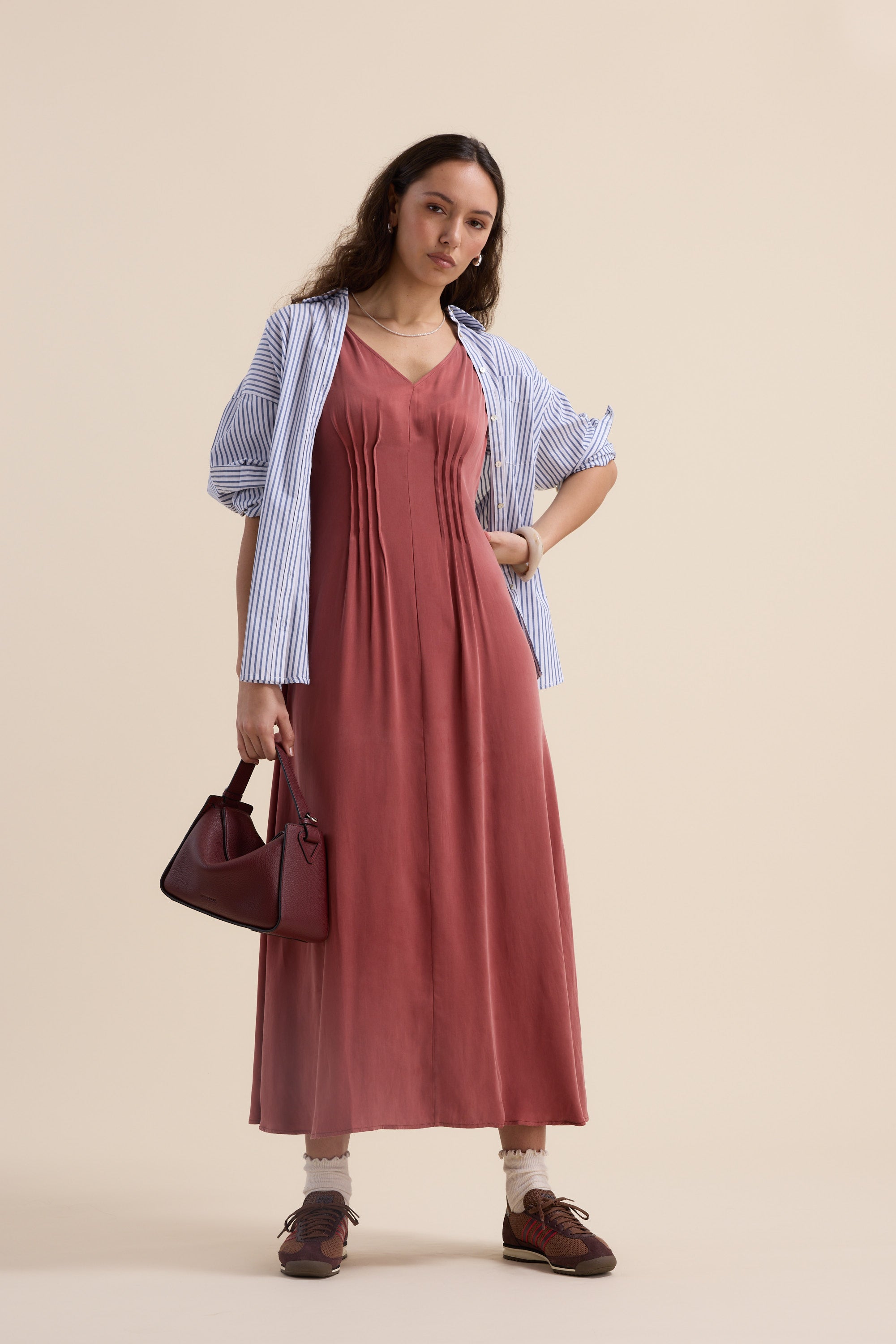 Woman in Max Cara Pleat Detail Dress, striped shirt, with handbag, against beige background.