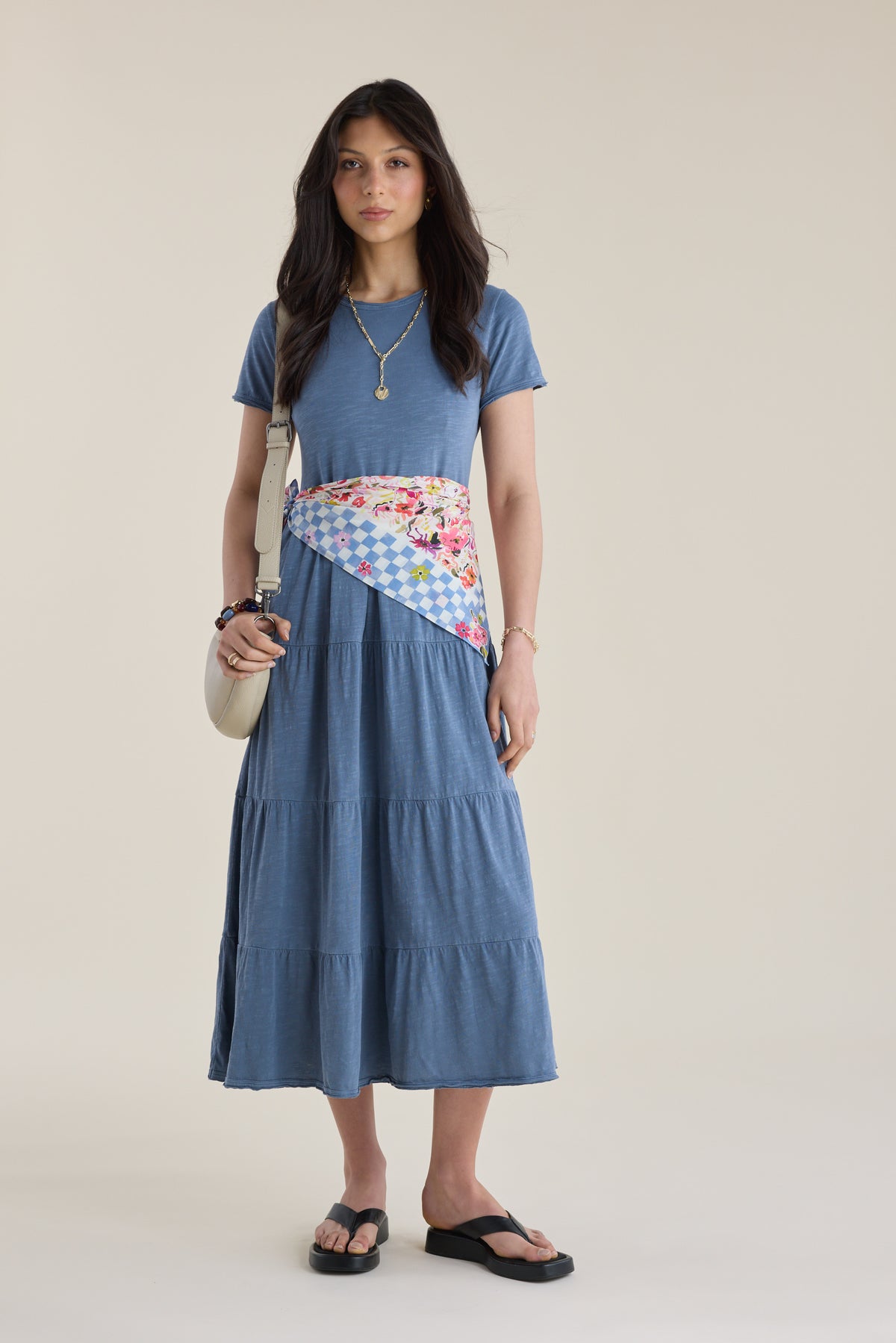 Woman in an Elementary Jersey Tiered Dress, floral waist scarf, sandals, necklace, and purse.