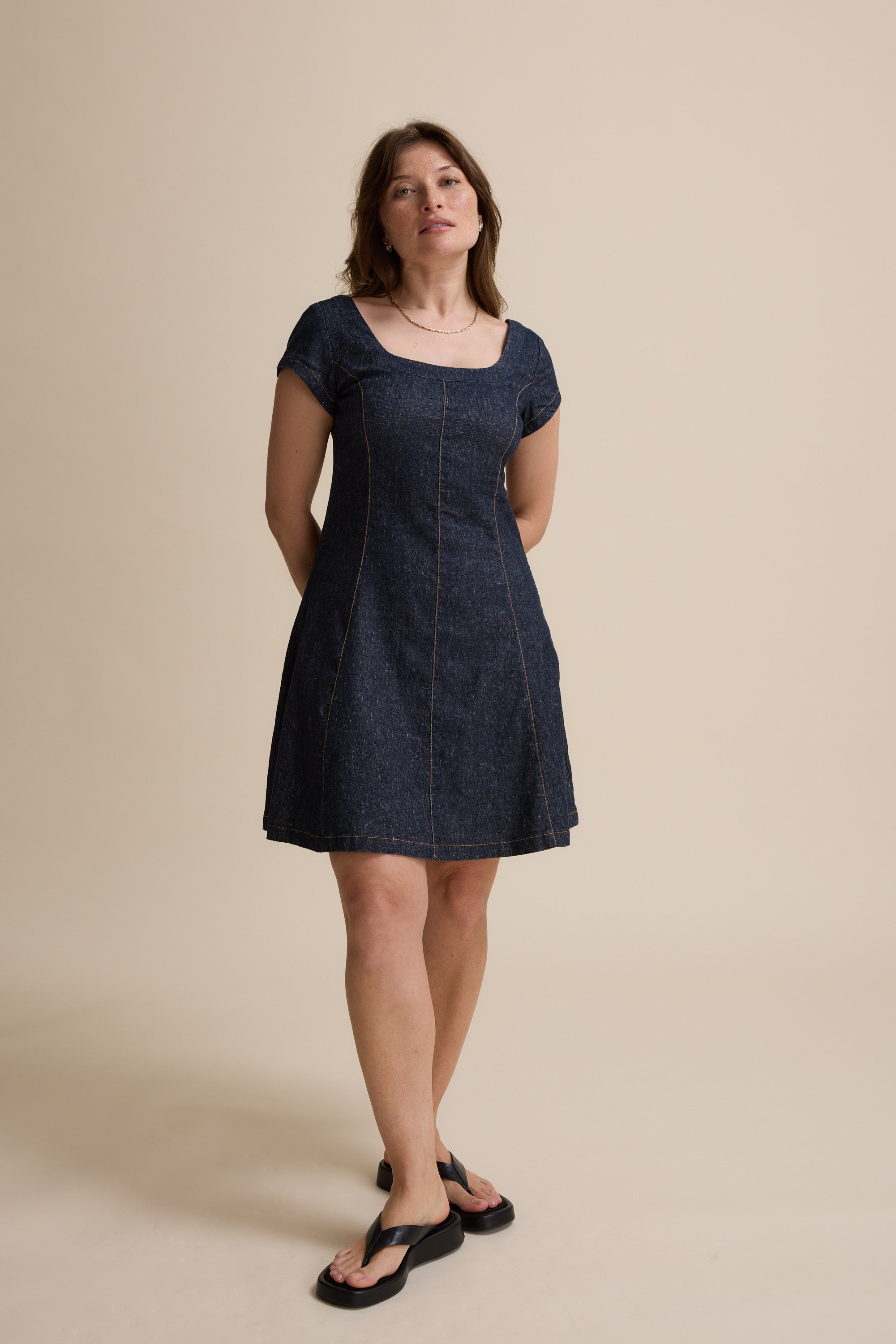Woman in The Linen Studio Cap Sleeve Dress by Max and sandals against a beige background.