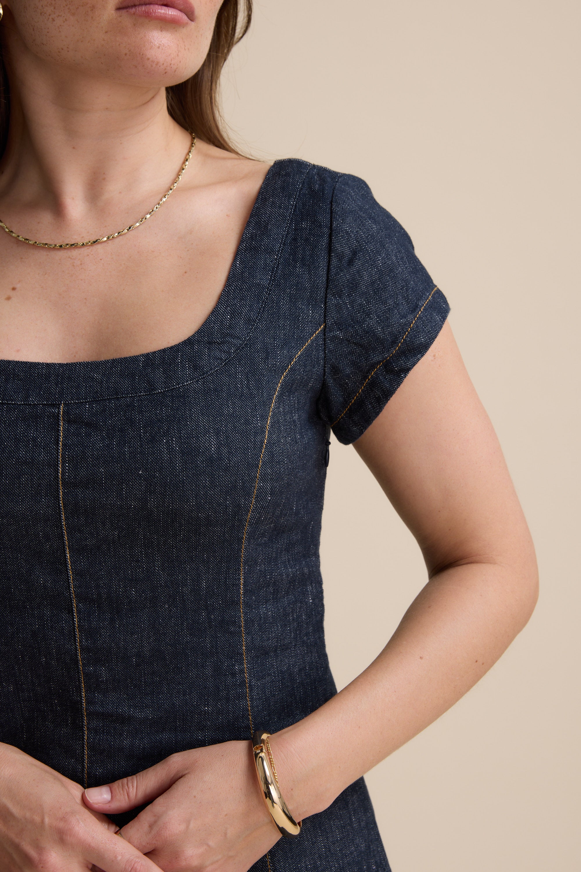 Woman in The Linen Studio Cap Sleeve Dress by Max, shoulders to waist, beige background.