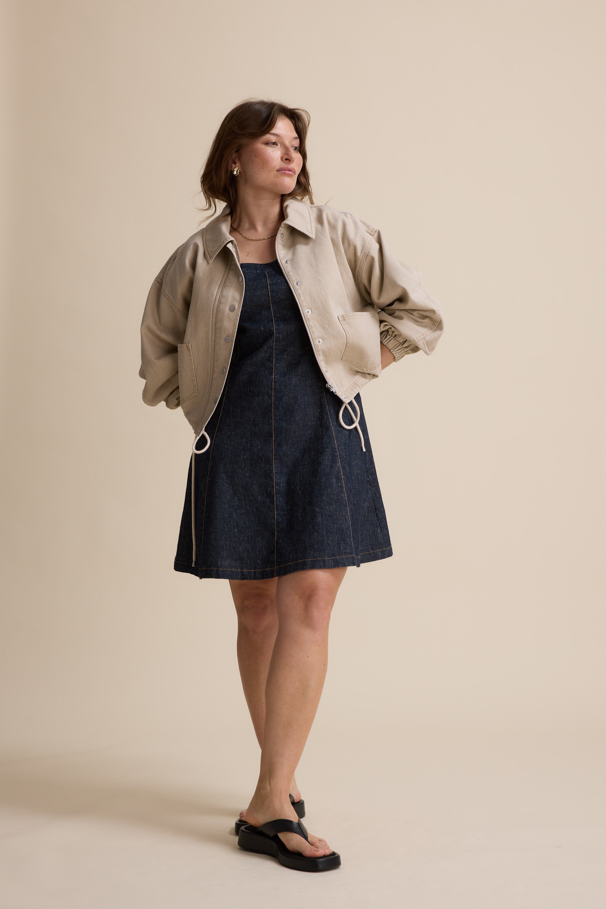 Woman in The Linen Studio Cap Sleeve Dress by Max and black sandals on a beige background.