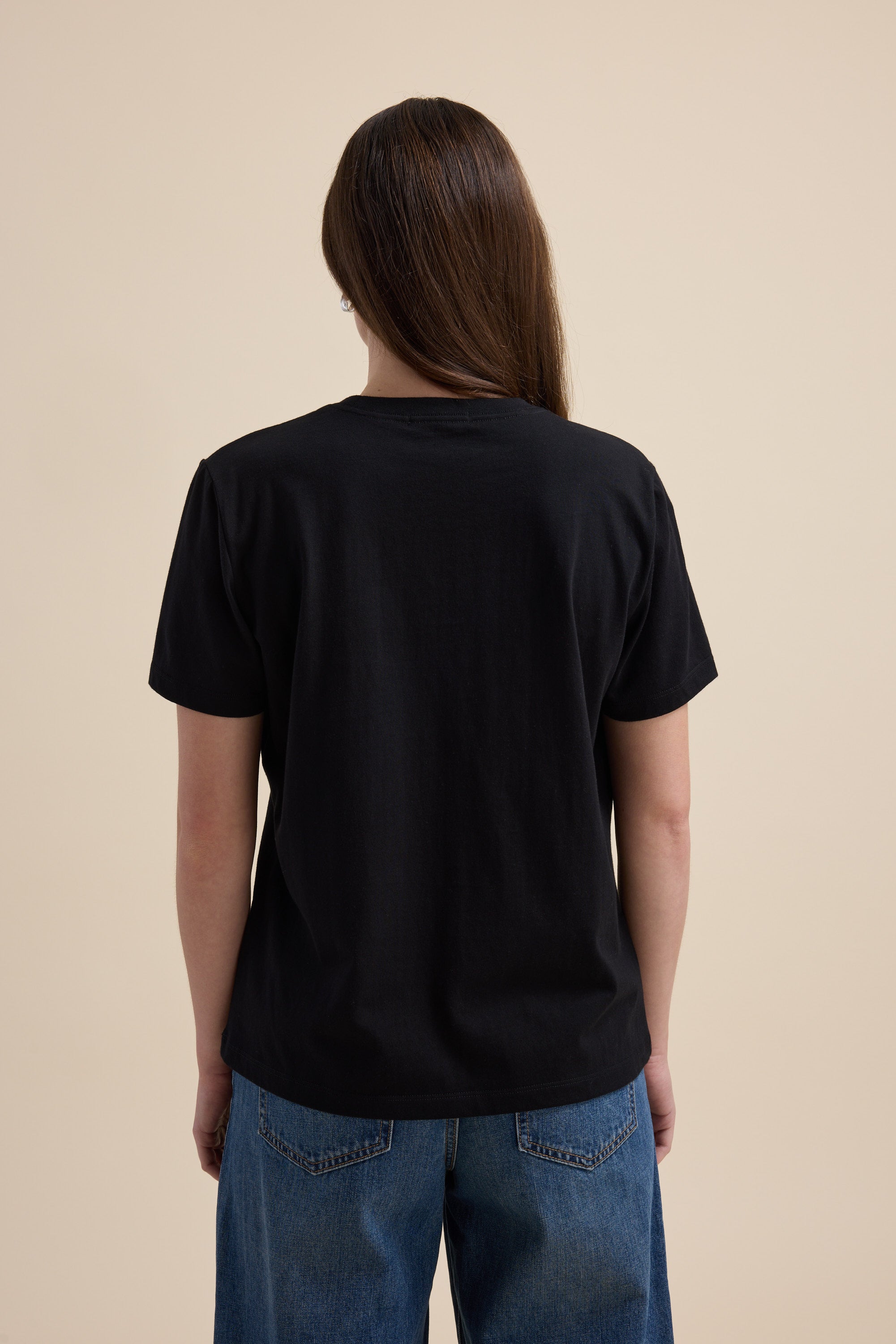 Person with long brown hair wears Max's The Good Earth Cotton Crew Tee, seen from behind.