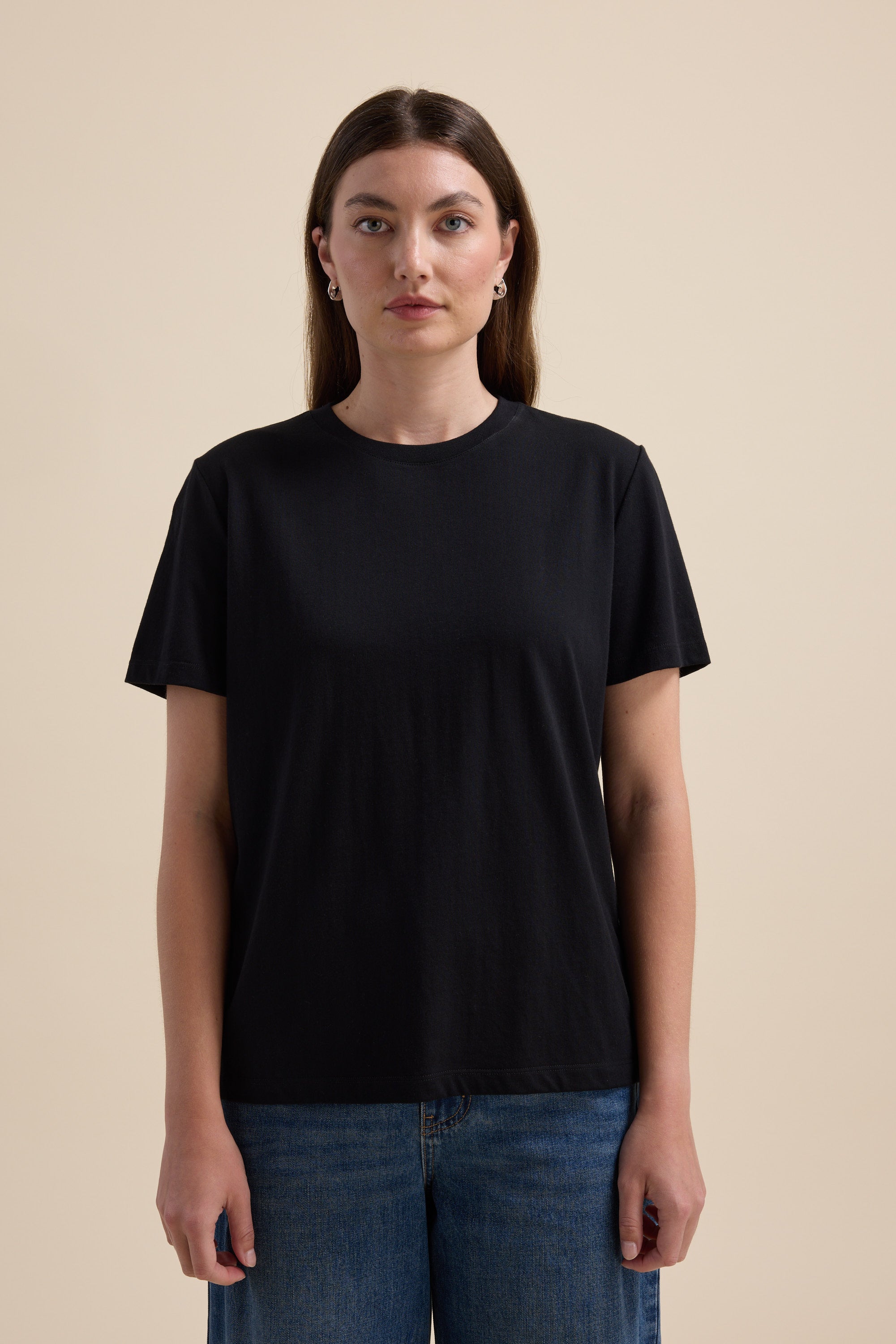 Woman wears Max's The Good Earth Cotton Crew Tee in black and blue jeans, beige background.