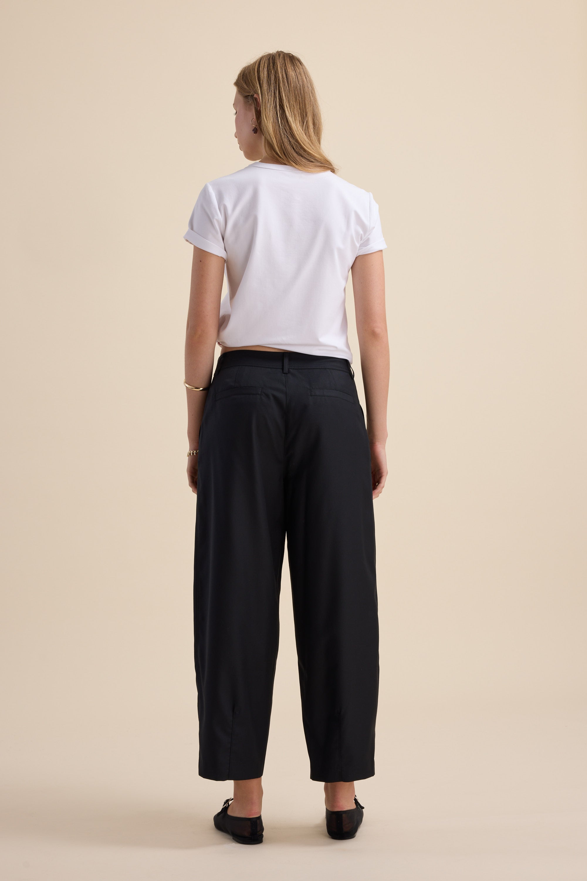A woman wears Max's The Wool Blend Barrel Leg Pants and a white T-shirt, facing away.