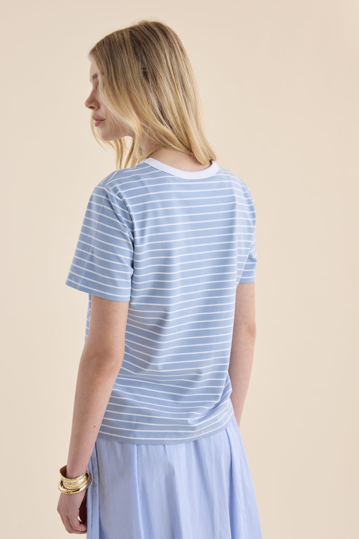 Woman in Max’s Perfect SS Crew Neck Tee, light blue stripes, skirt, bracelets on left wrist.