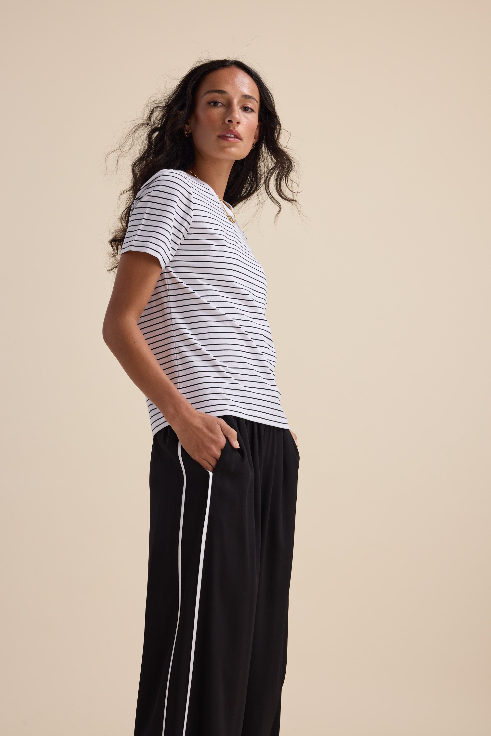 Woman in Max The Perfect Short Sleeve Crew Neck Tee and black pants with white stripes, sideways.