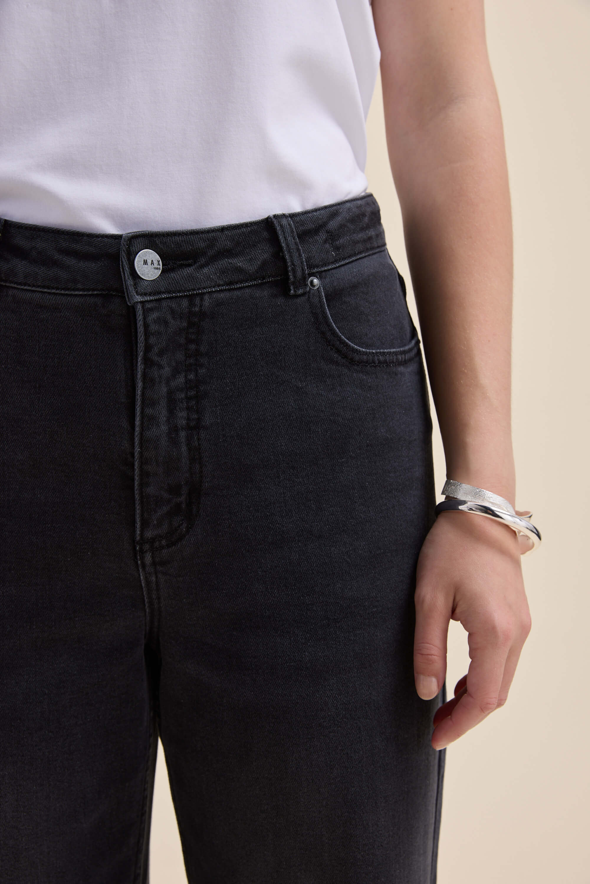 Person wears Max’s The Mid Rise Wide Leg Jeans, a white shirt, and a silver bracelet on right wrist.