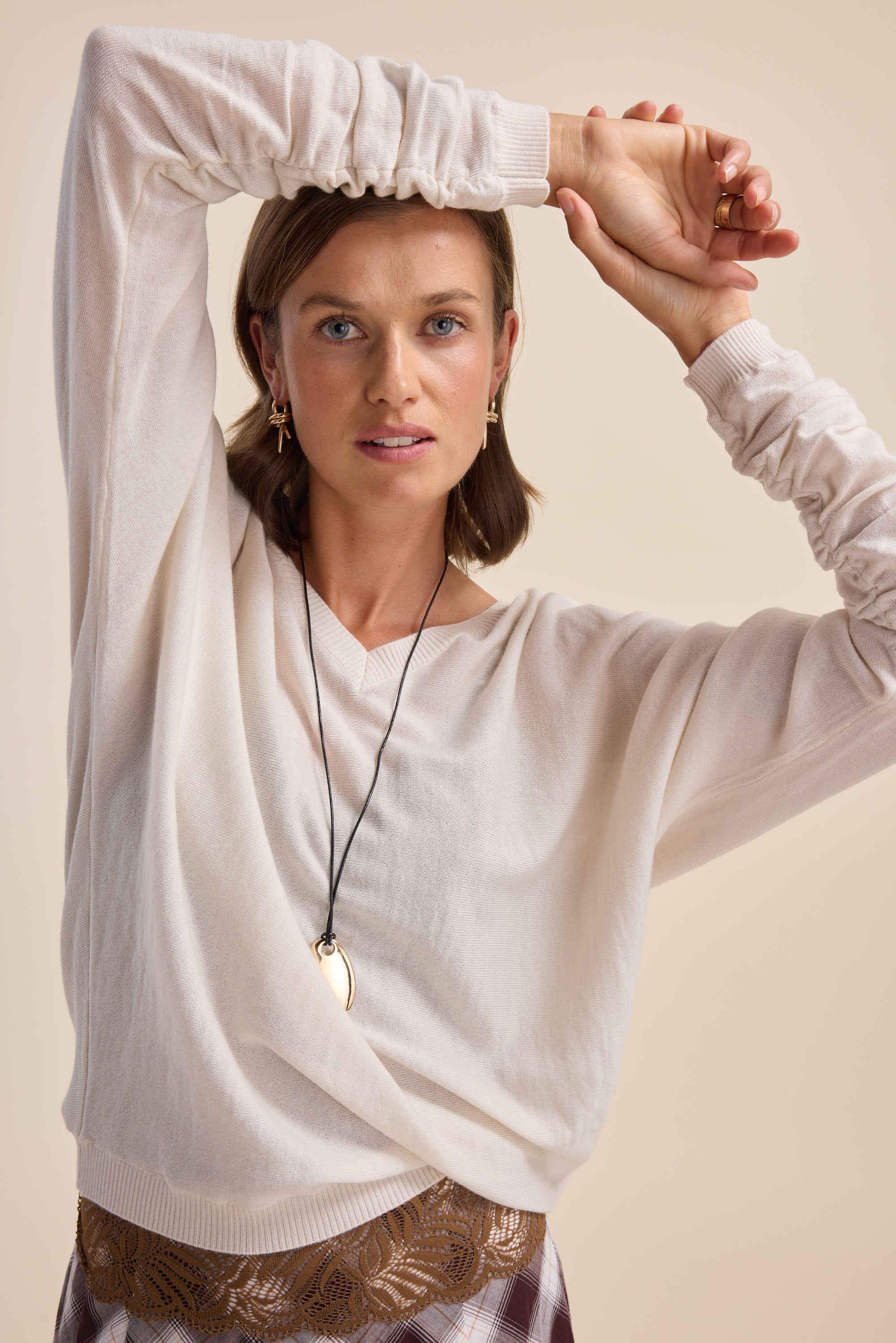 Woman in Elementary ZQ Merino Reversible Sweater poses with one arm raised, wearing a necklace.