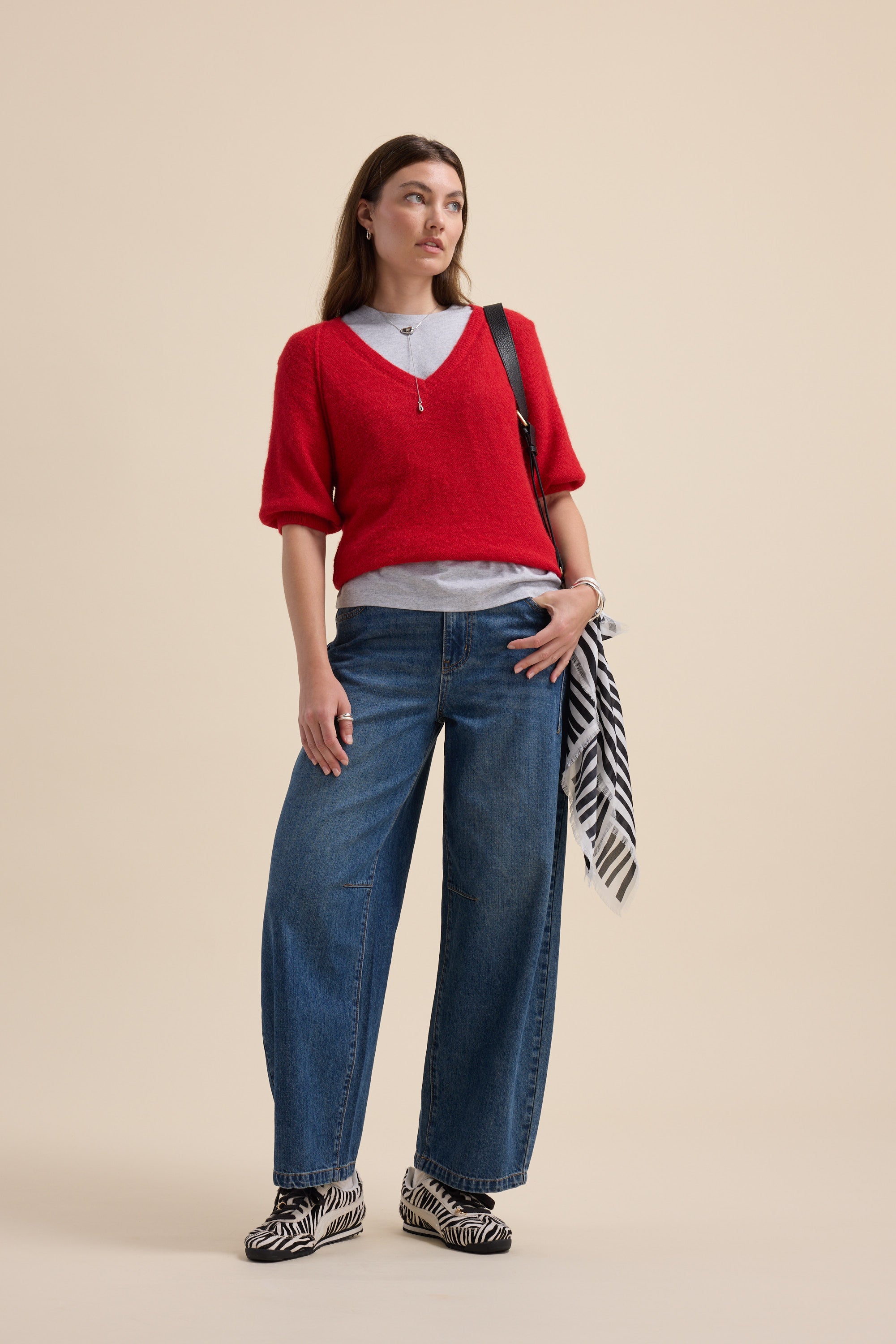 Woman in a red Max Ivy Knitted V Neck Tee, wide-leg jeans, zebra shoes, and holding a striped scarf.