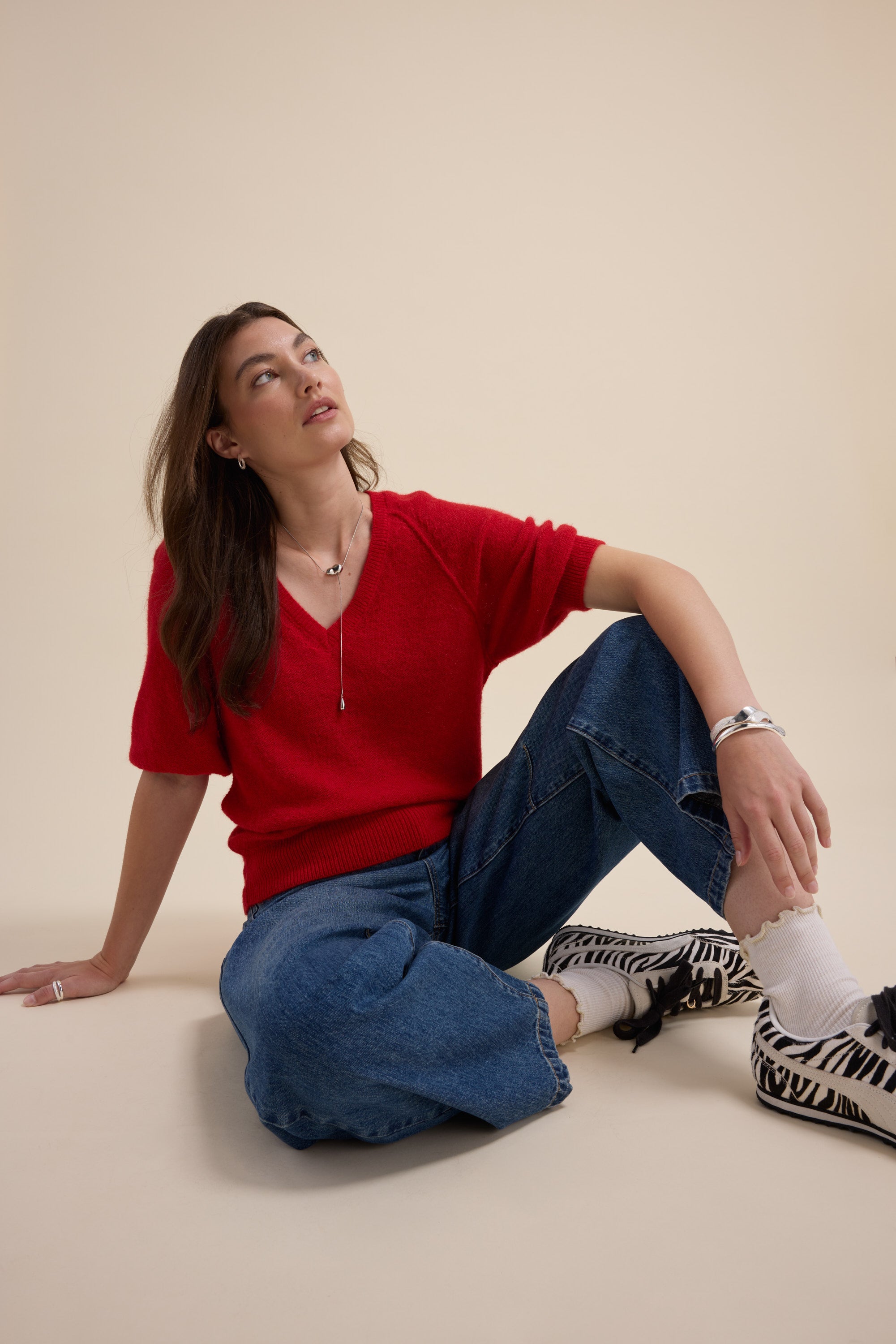 Woman in Max Ivy Knitted V Neck Tee and jeans sits on the floor in zebra print shoes.