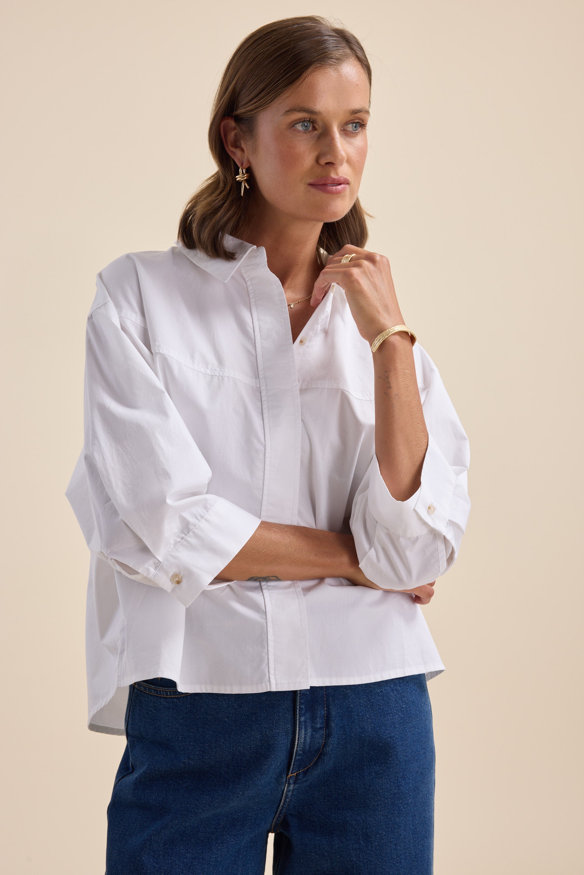 Woman in an Elementary Yoke Detail Shirt and blue jeans, standing thoughtfully.