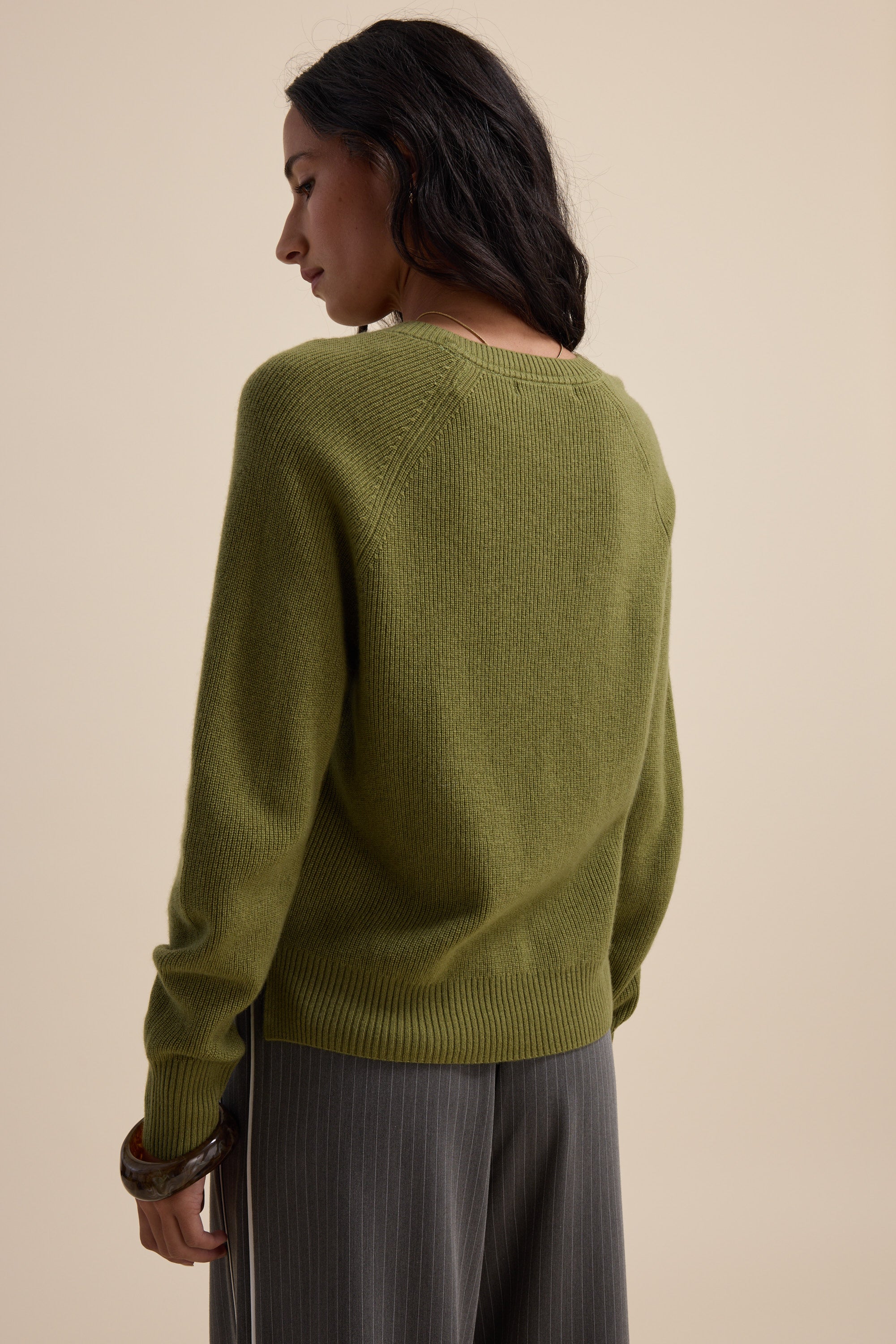 Woman in an Elementary Cashmere Blend V Neck Sweater and gray pinstripe pants, standing away.