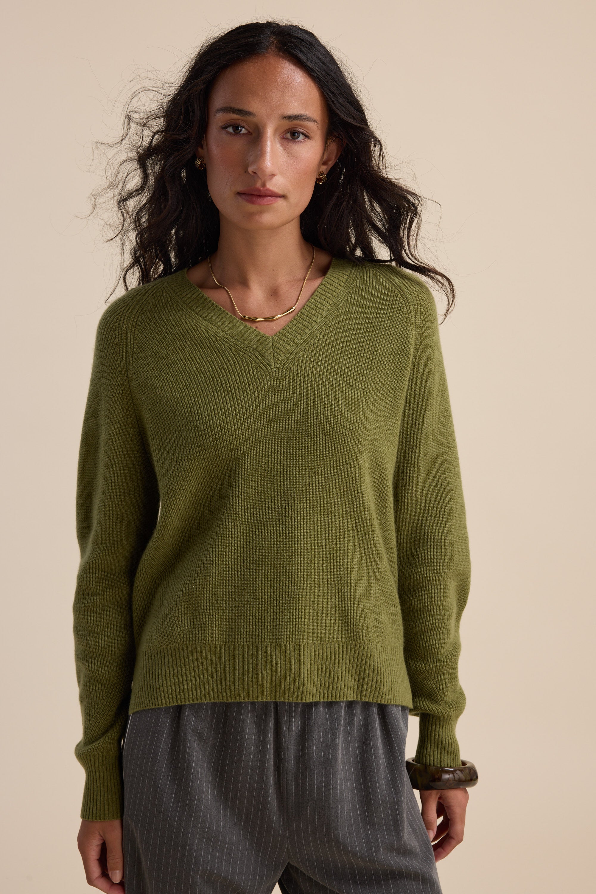 Woman in an Elementary Cashmere Blend V Neck Sweater and gray pinstripe pants stands against beige.
