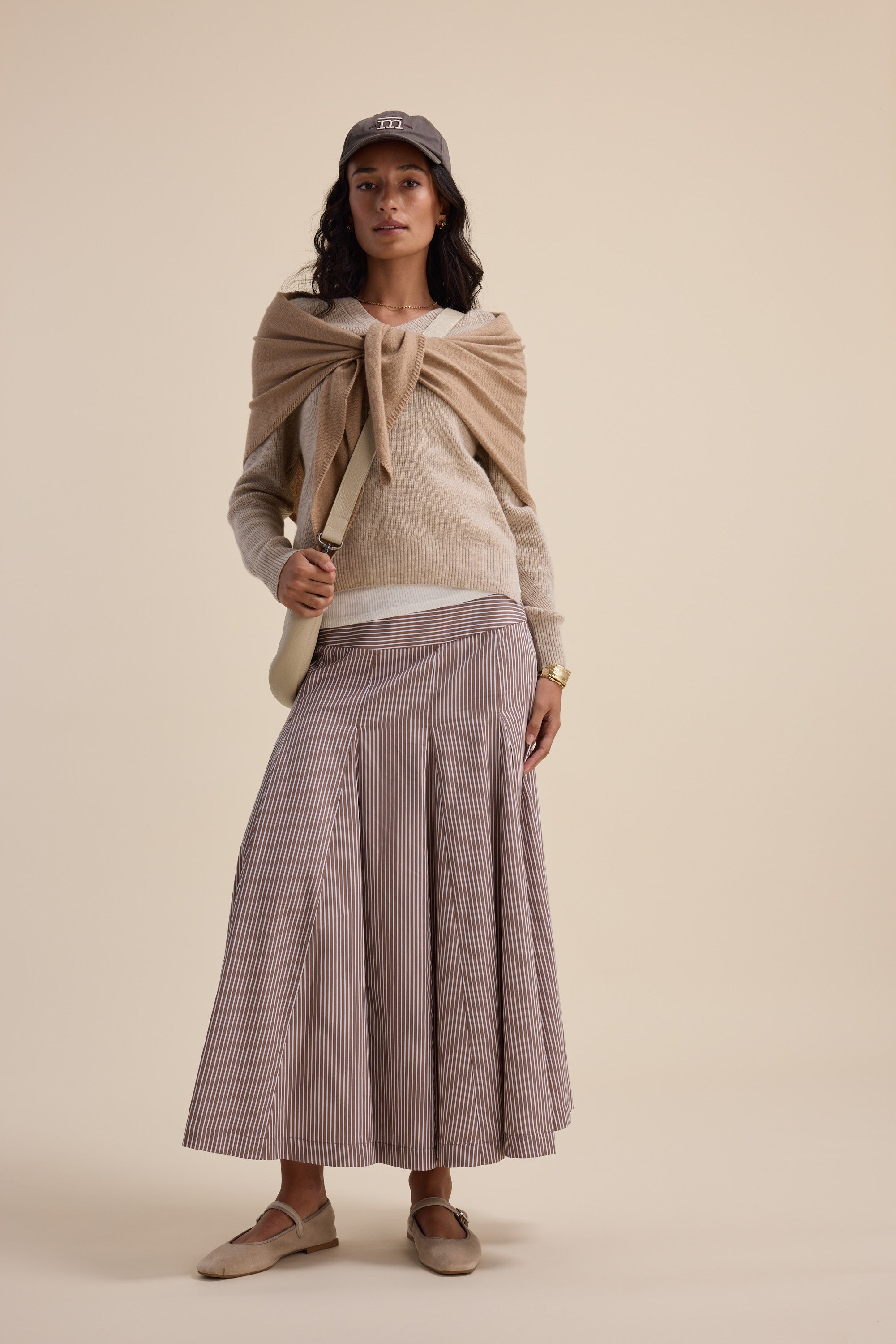 Woman in neutral tones, wearing Elementary V Neck cashmere blend sweater, knit skirt, and loafers.