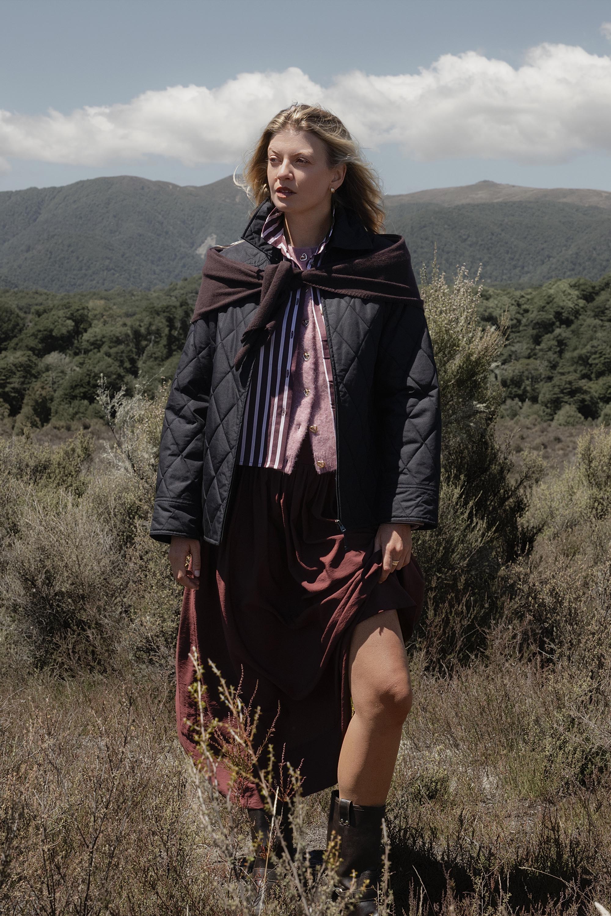 Woman in the Elementary Quilted Puffer walks in grassy, mountainous surroundings.