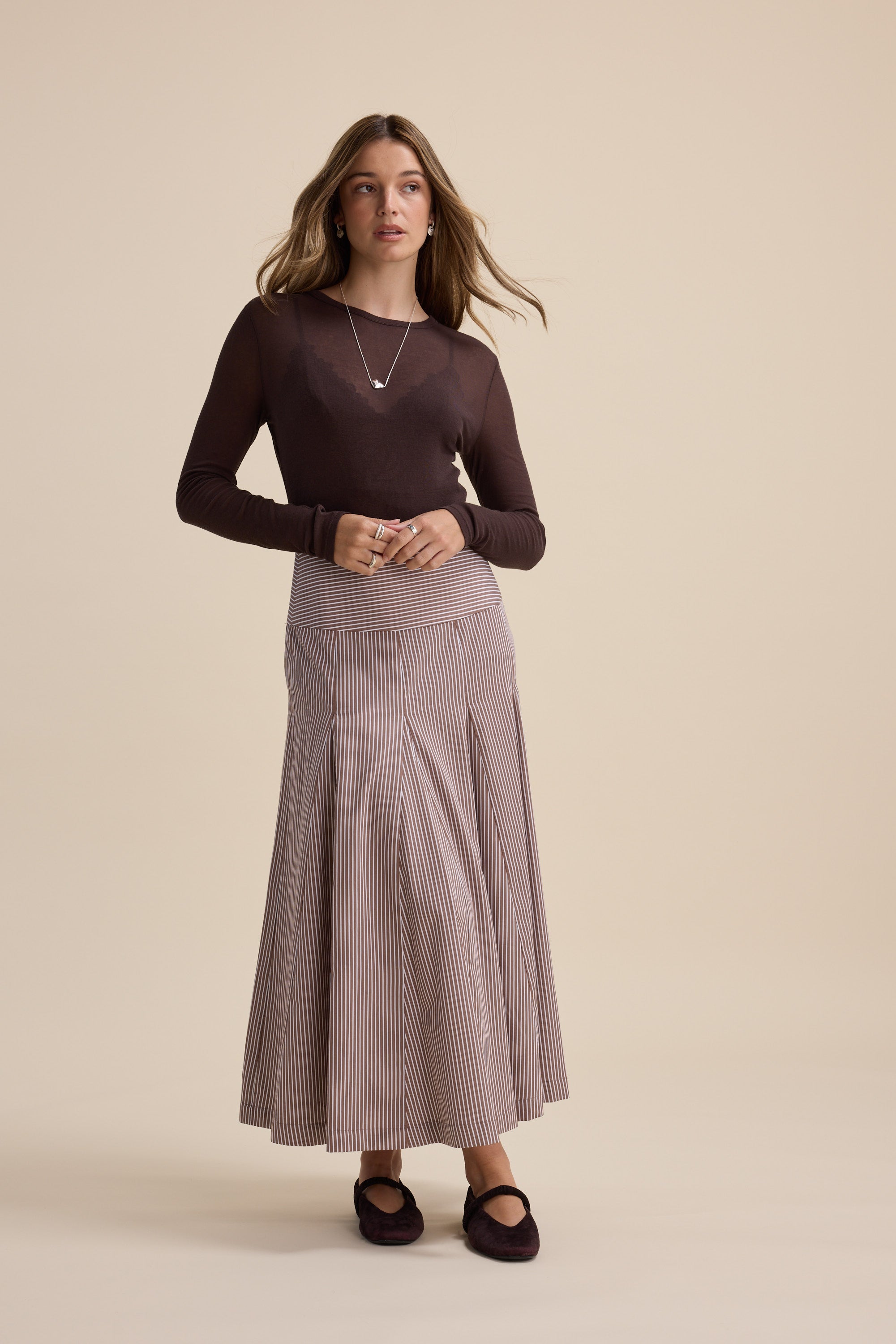 Woman in a brown top and Max Marley Panel Seam Skirt against a beige background.